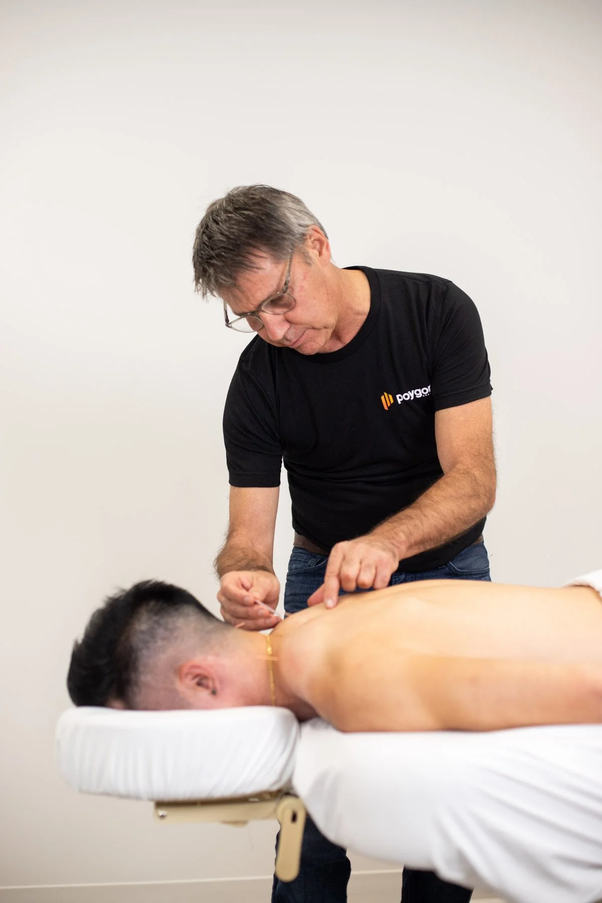 A man receiving a massage on his back in a clinical setting with white walls.