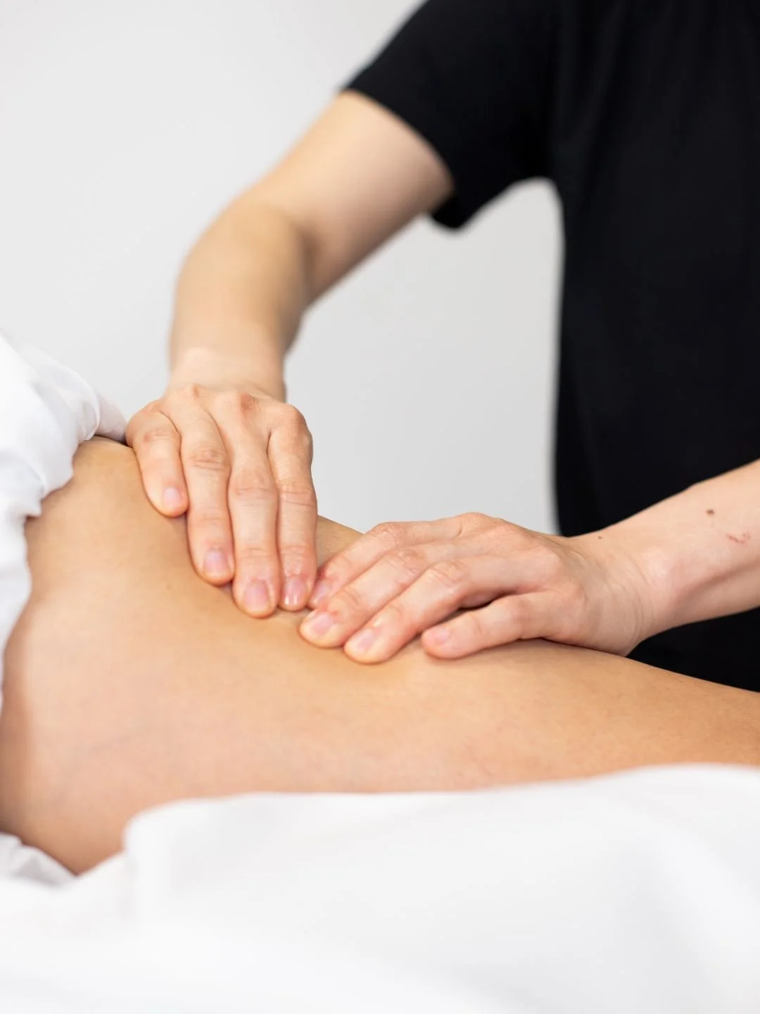 A woman providing physical therapy or injury treatment to a person lying on a table, wearing a black t-shirt with a logo, in a clinical setting.
