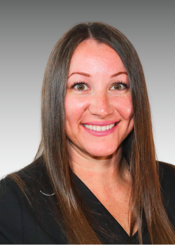 A woman with long brown hair smiling, wearing a black top, against a gray background.