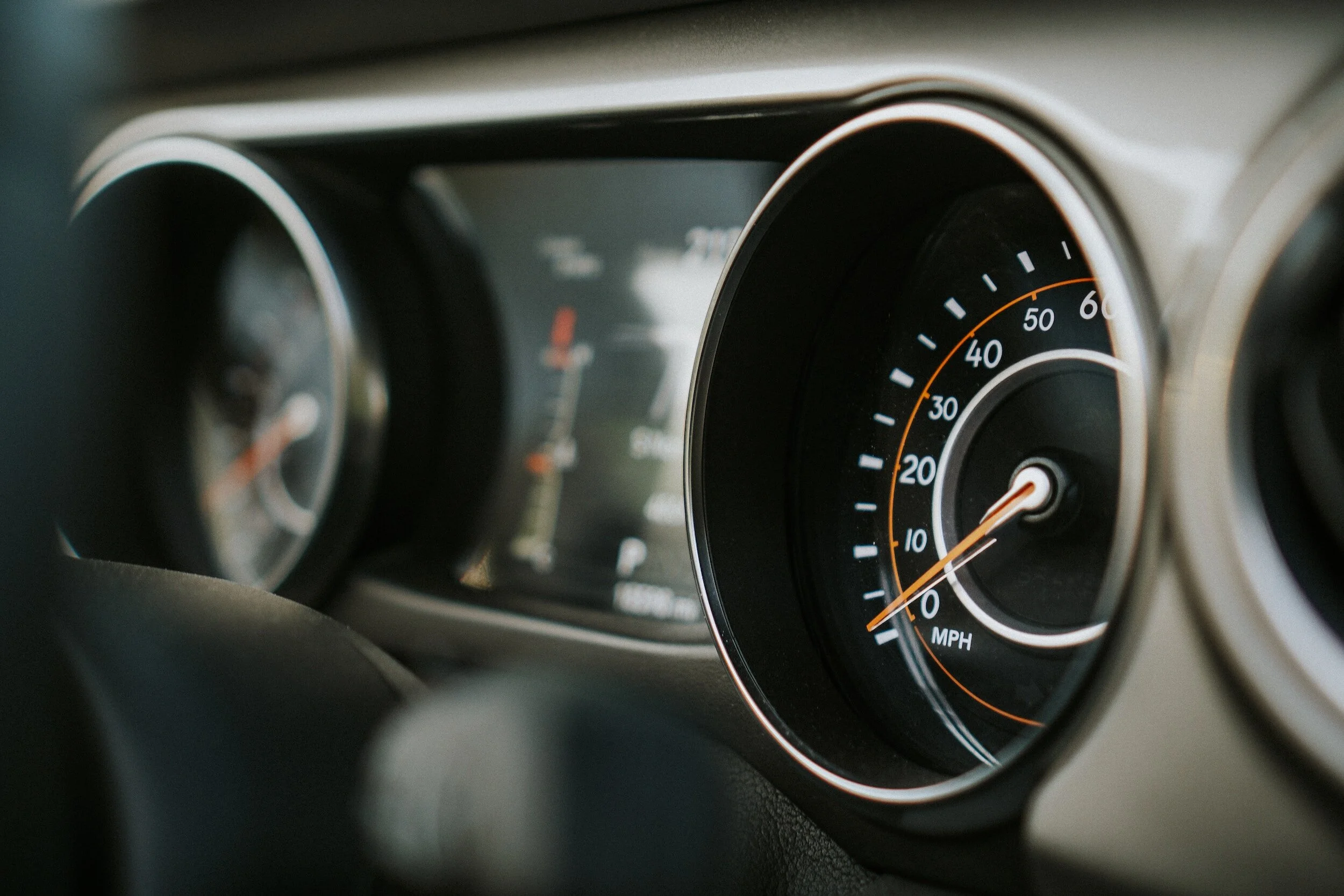 Close-up of a car dashboard showing a speedometer with orange needle pointing at zero and other gauges.
