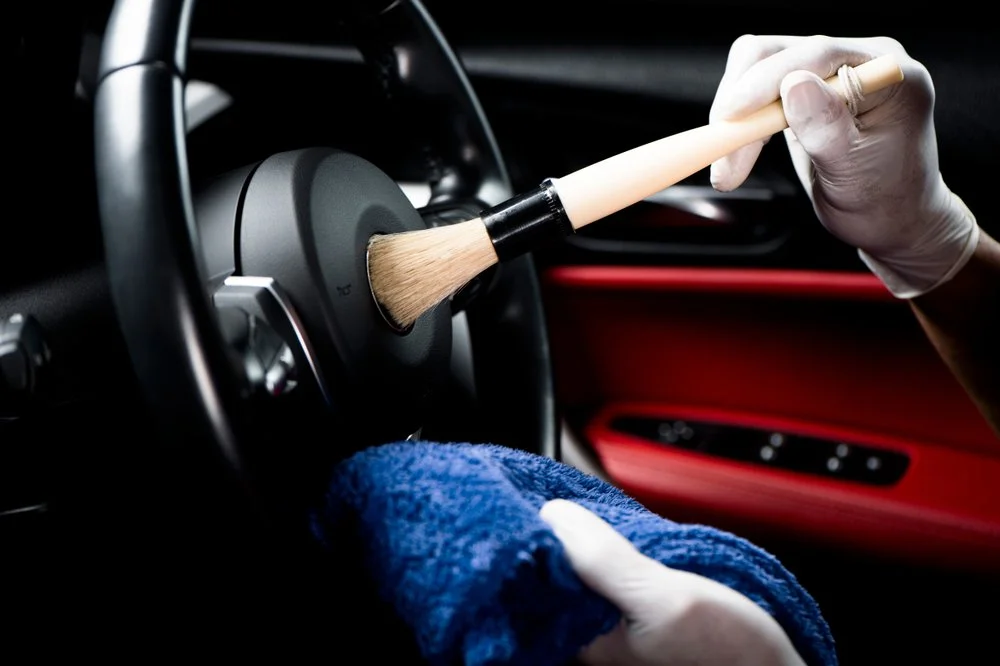 Person cleaning car steering wheel with brush and towel