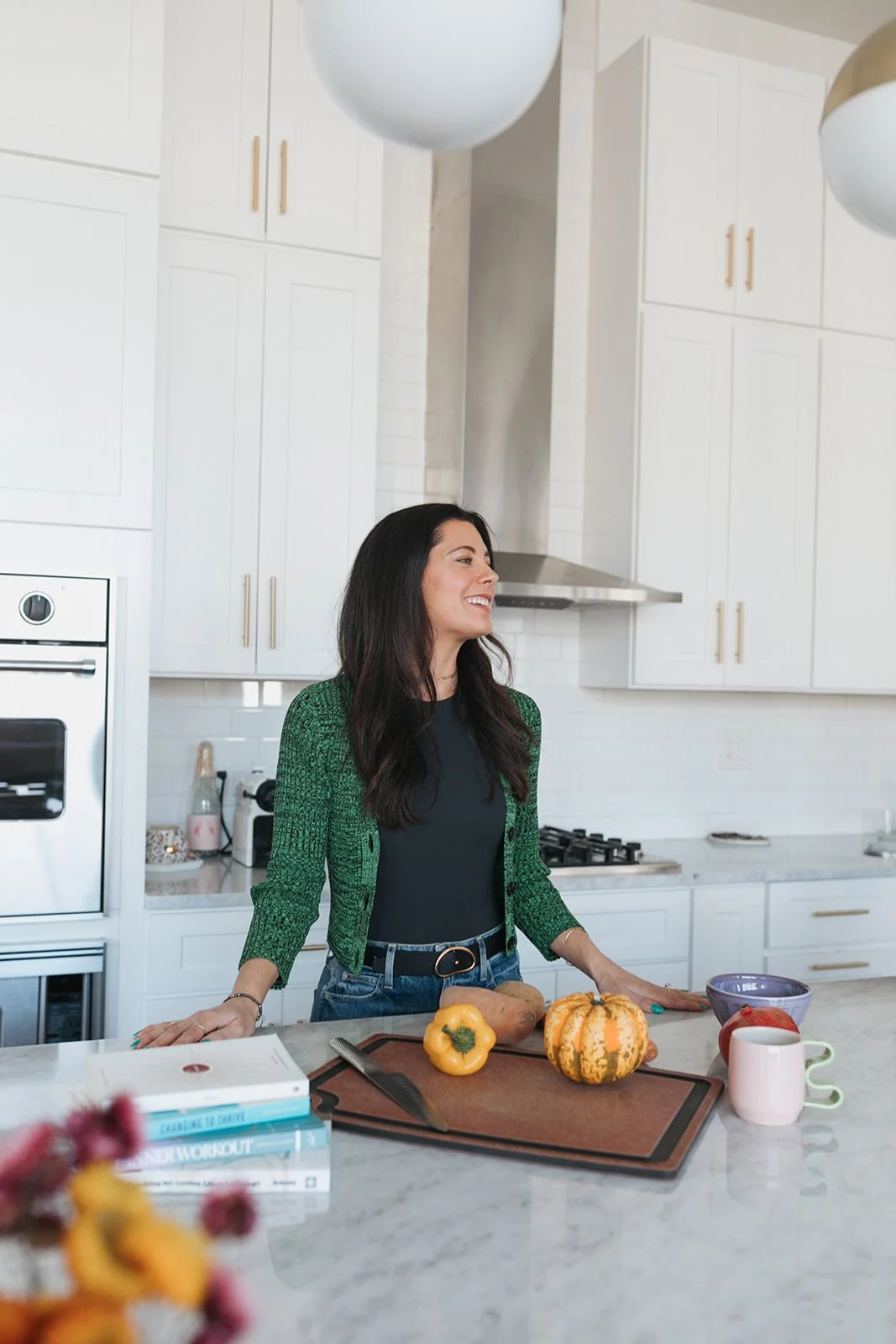 Woman in kitchen with vegetables on countertop, knife, books, and a pink mug.