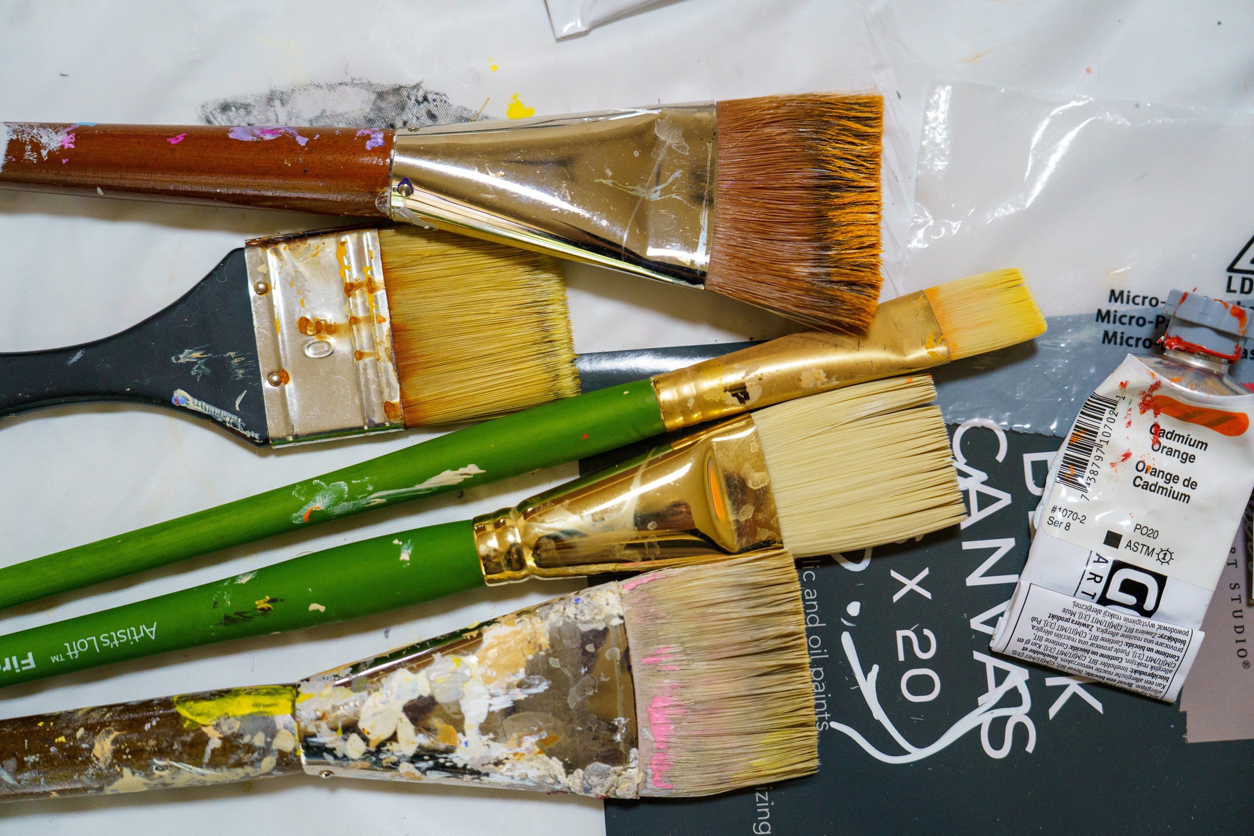 Several paintbrushes of different sizes are placed on a surface along with a tube of paint.