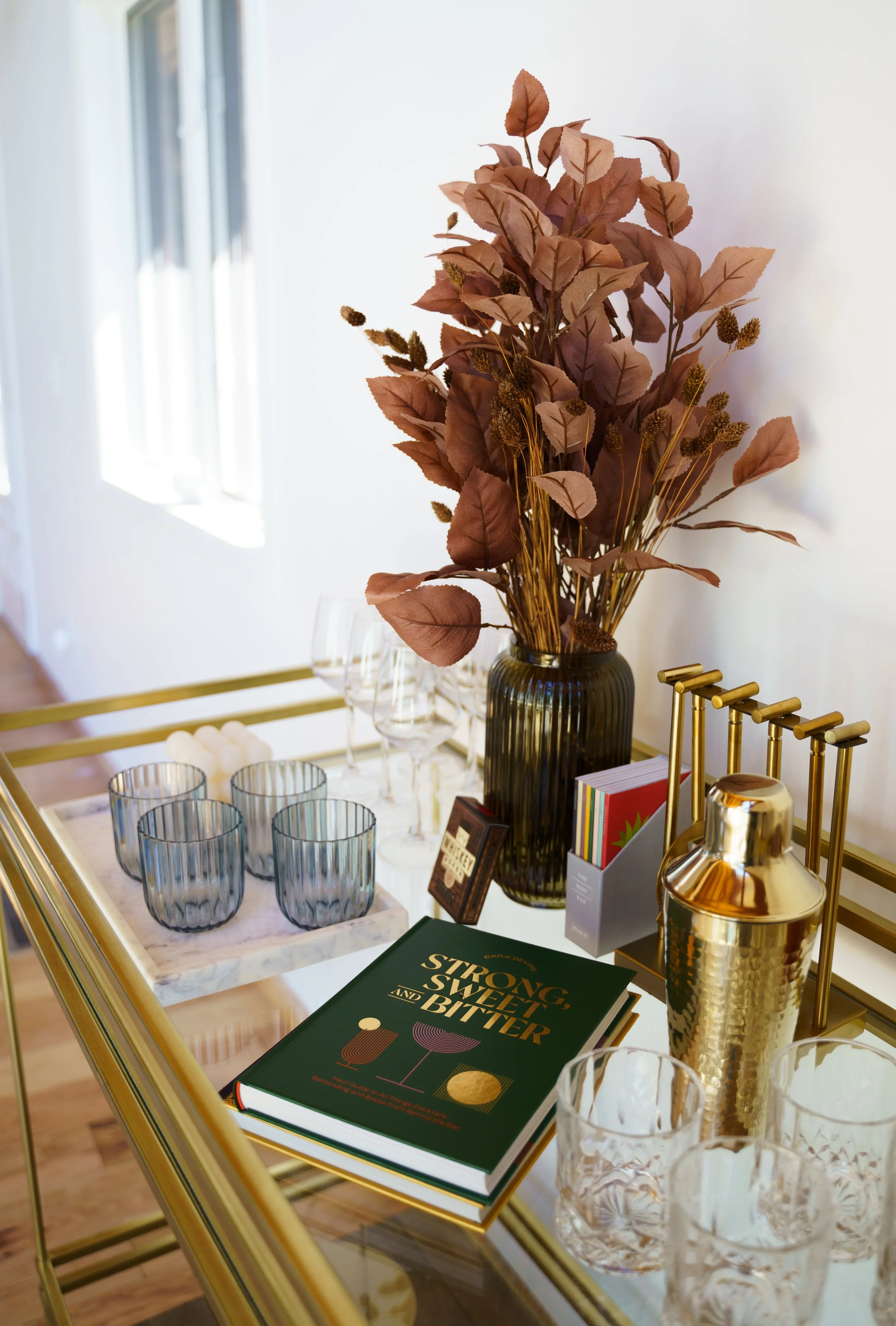 Top down photo of a bar cart with wine glasses, tumblers, cocktail books, a plant, and bar tools