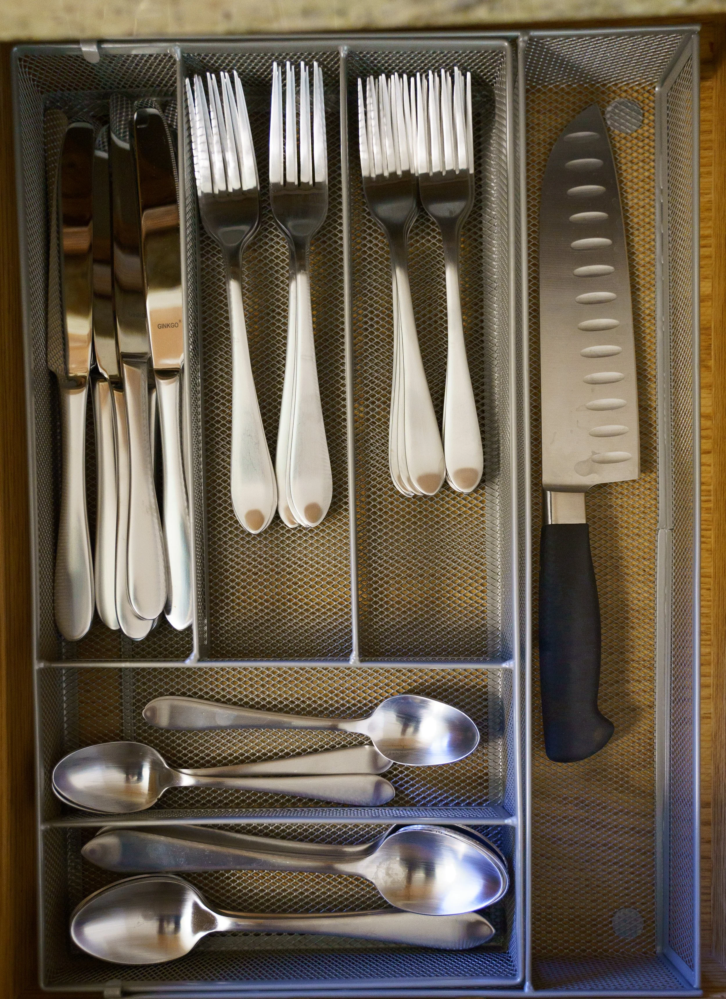 Top down photo of a drawer full of silverware and a kitchen knife.