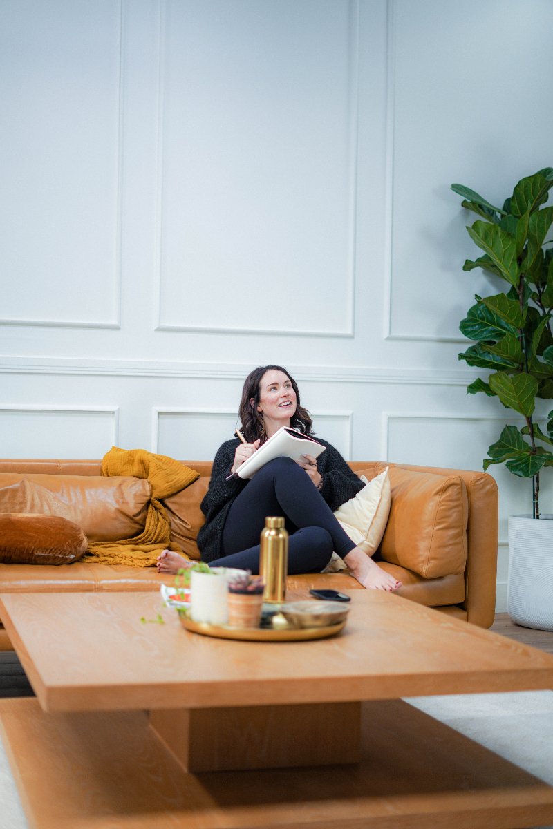 Chelsea Quint sketching out a decision fatigue audit in her notebook, sitting on a leather couch with a journal and pen in hand.