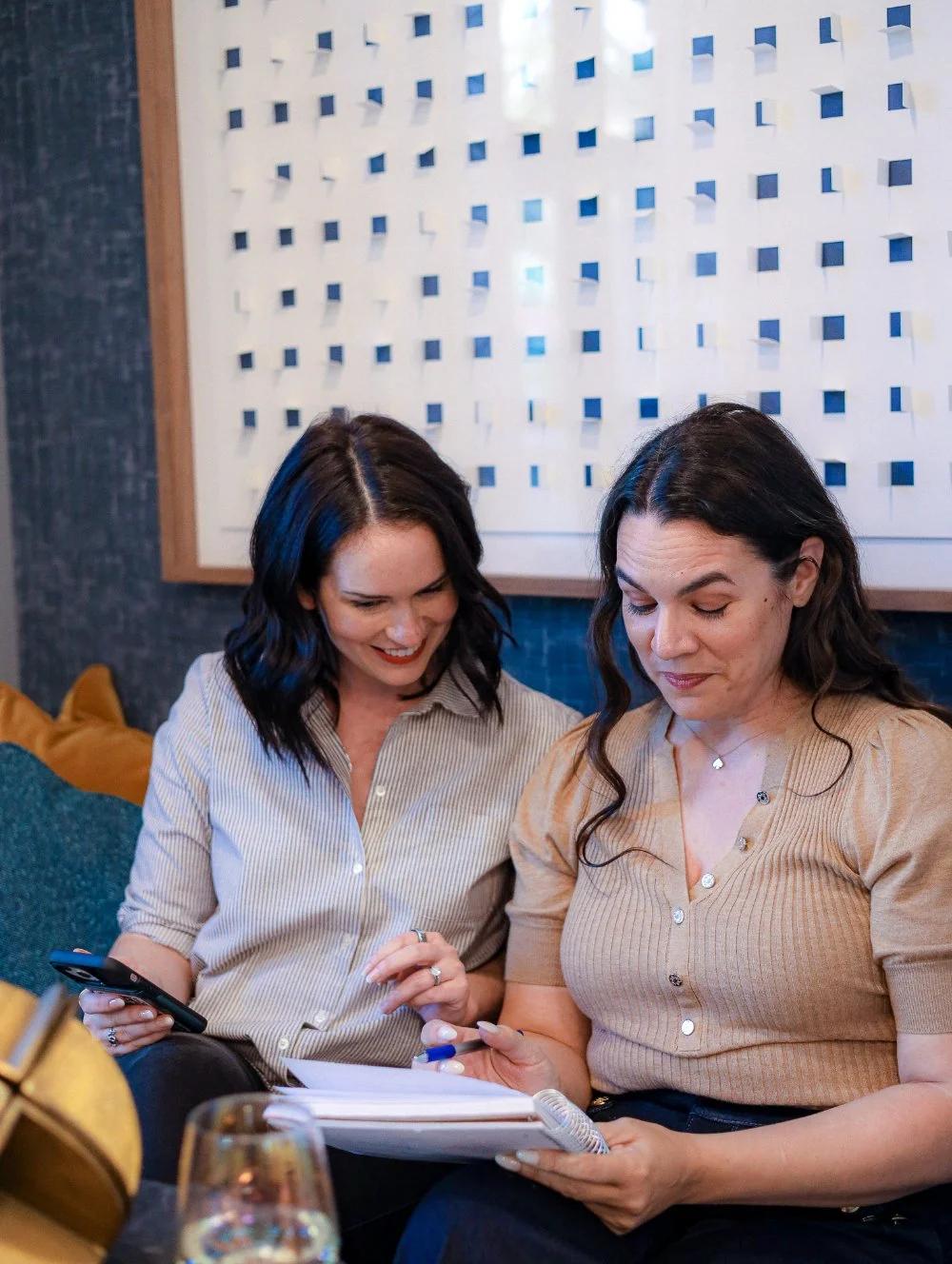 Two women reviewing notes together on a couch, collaborating on business strategy and problem-solving during a low sales period.