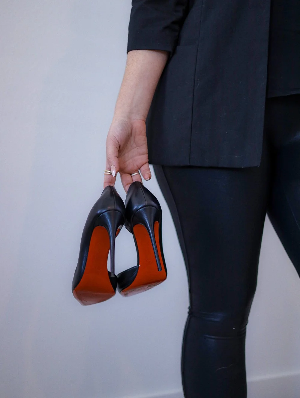 A woman in sleek black attire holds a pair of heels, blending professionalism with personality—an understated nod to confidence, presence, and showing up fully in business.