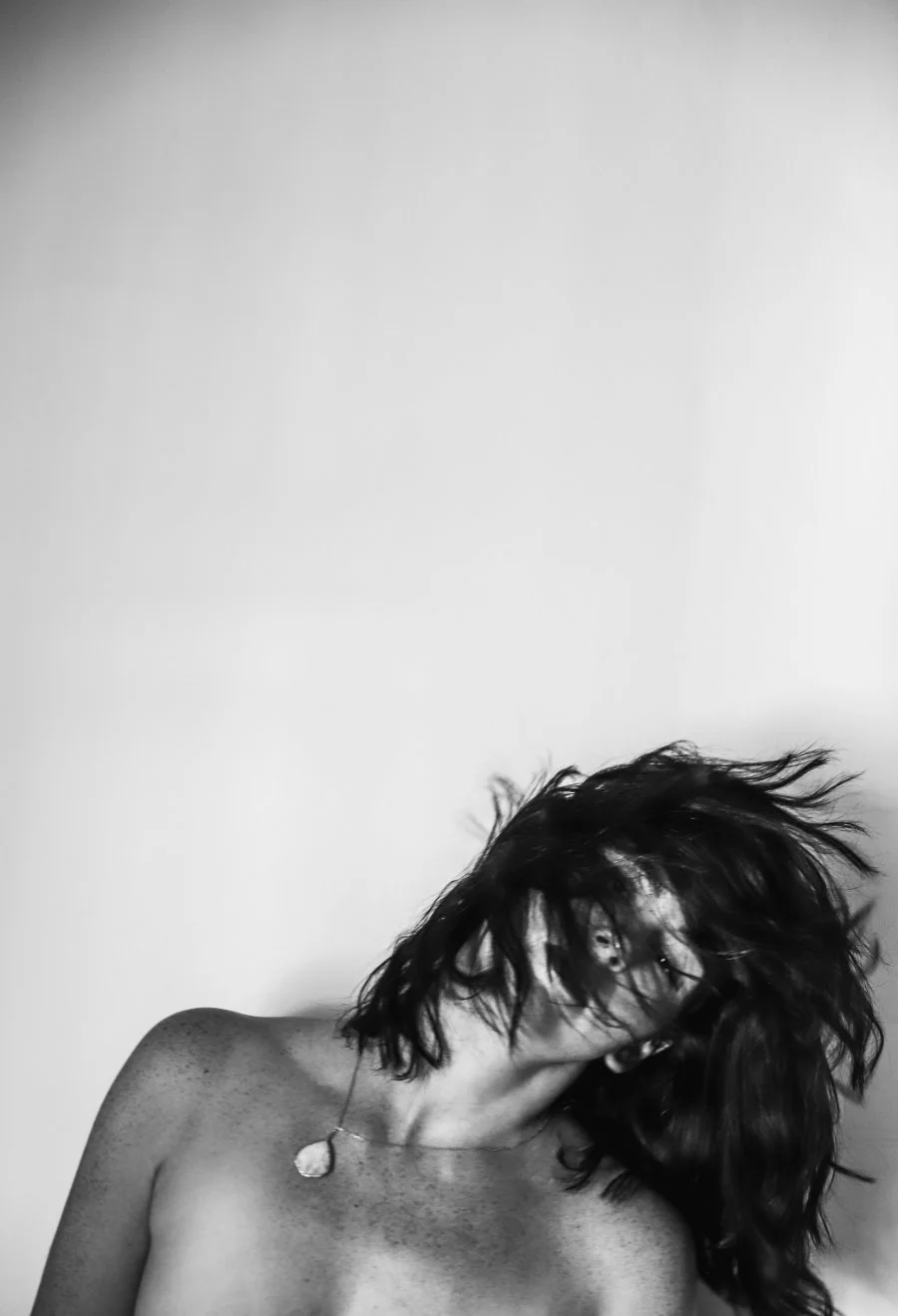 Black-and-white photo of a woman flipping her hair mid-motion, minimal backdrop, capturing a bold, in-between moment that reflects the reset energy of a mid-year company audit.