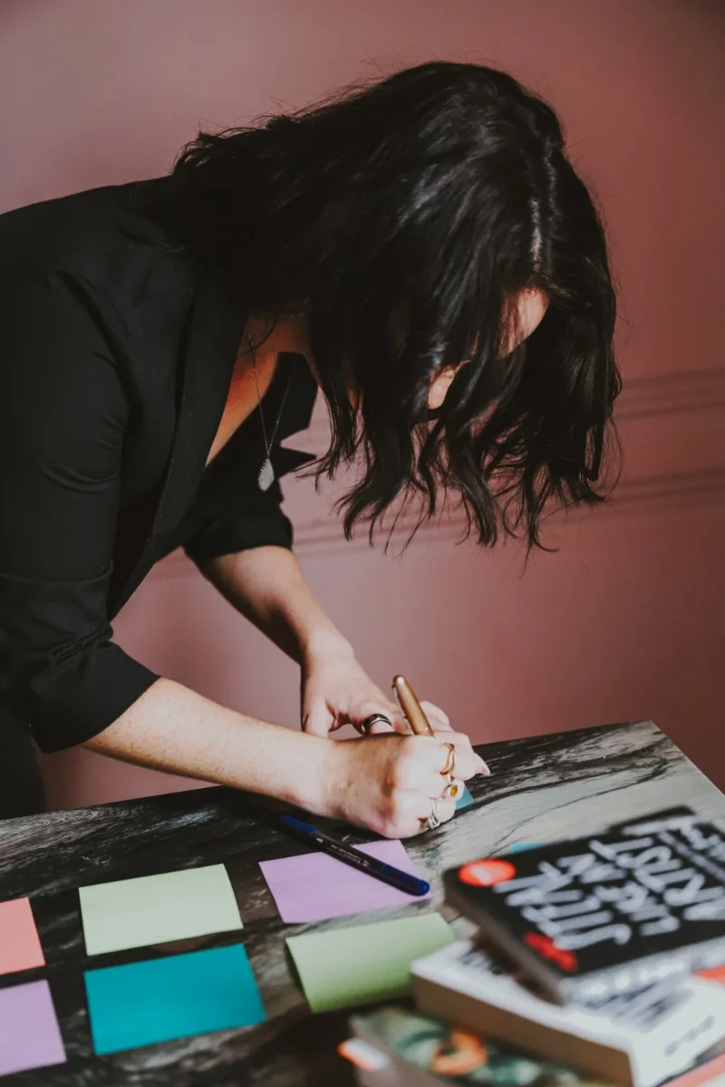 Chelsea Quint writing notes on colorful post-its at a marble desk, working through the messaging strategy behind an intangible offer.
