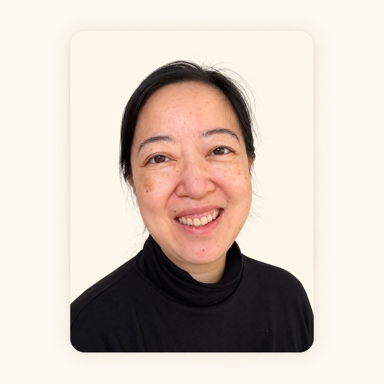 Smiling woman with short black hair wearing a black turtleneck against a white background.