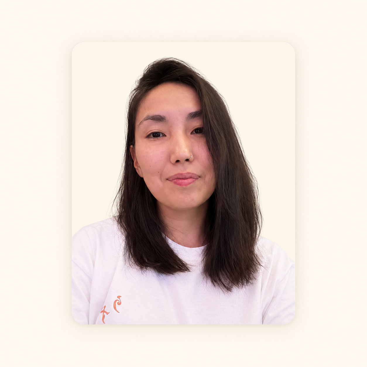 Close-up portrait of a young woman with medium-length dark brown hair, wearing a white t-shirt, smiling softly against a plain light-colored background.