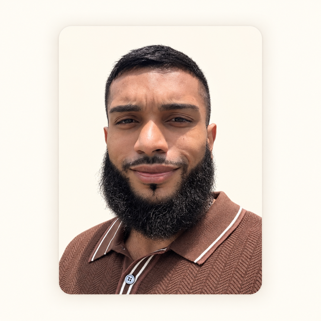 Close-up portrait of a man with a beard wearing a brown polo shirt with stripes, looking at the camera against a plain background.