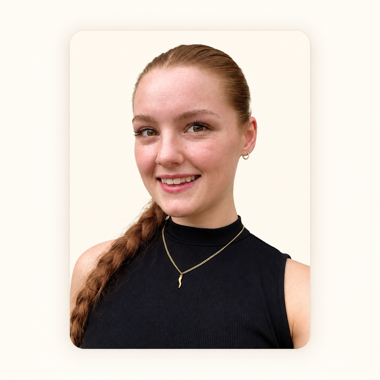 Young woman with red hair in braid, wearing a black sleeveless top, gold necklace, and silver hoop earrings, smiling against a neutral background.