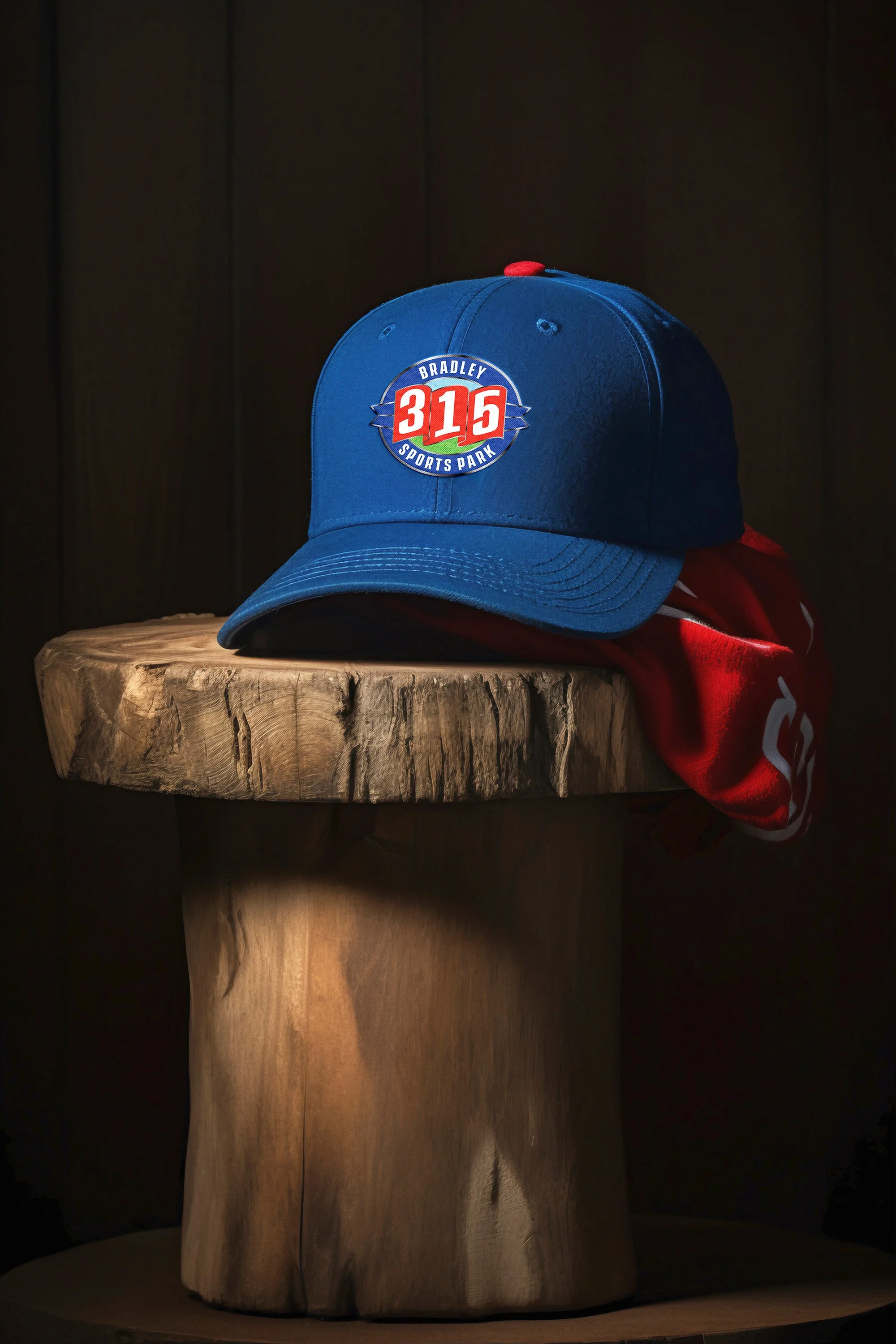 A blue baseball cap with a logo reading 'Bradley 315 Sports Park' placed on a wooden stand with a red item partially visible underneath.
