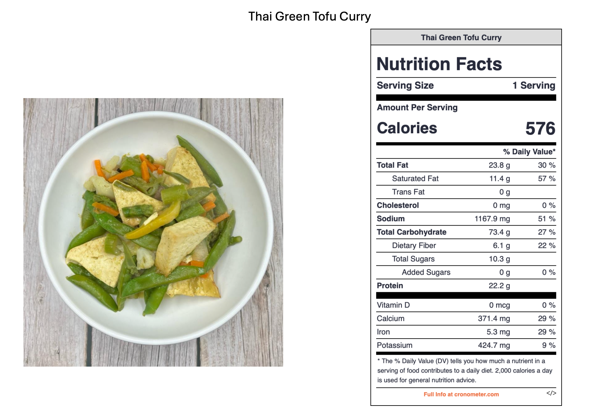 A bowl of Thai green tofu curry with green beans, carrots, and tofu on a wooden surface.