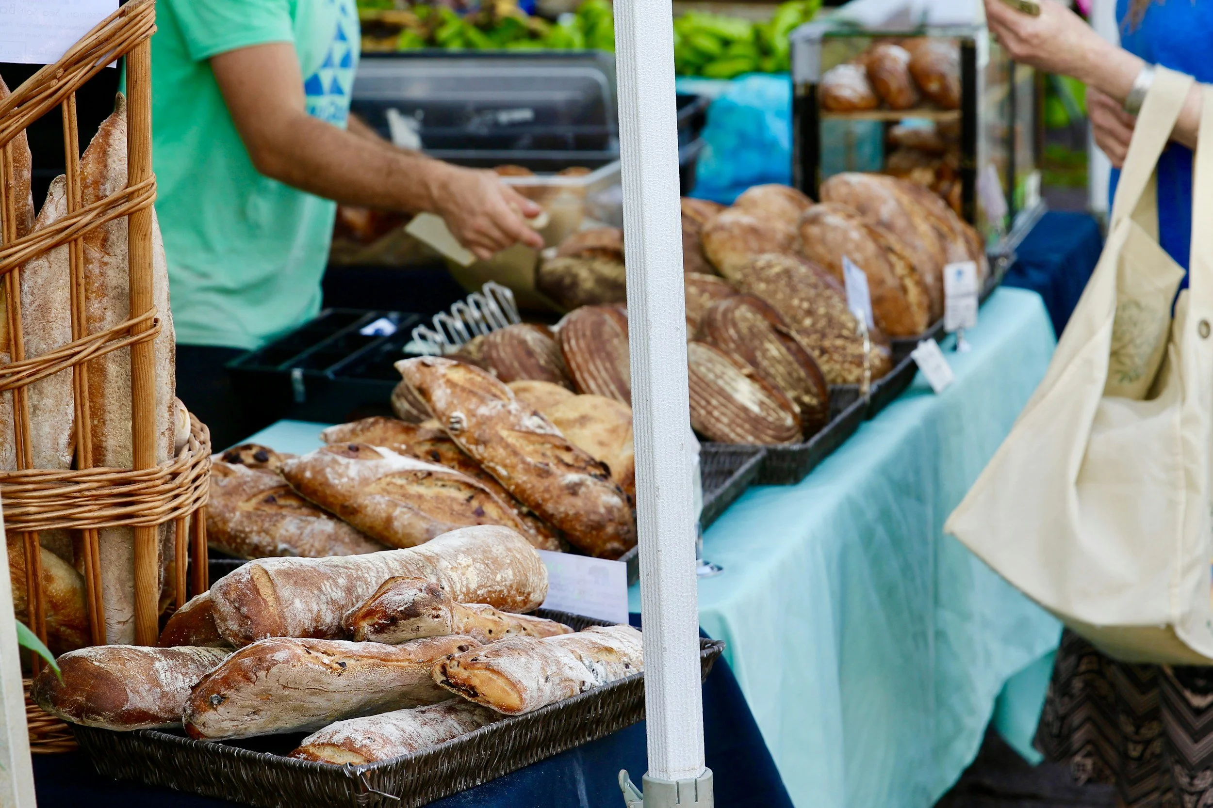 Baked bread and loaves displayed on a market stall with people shopping.