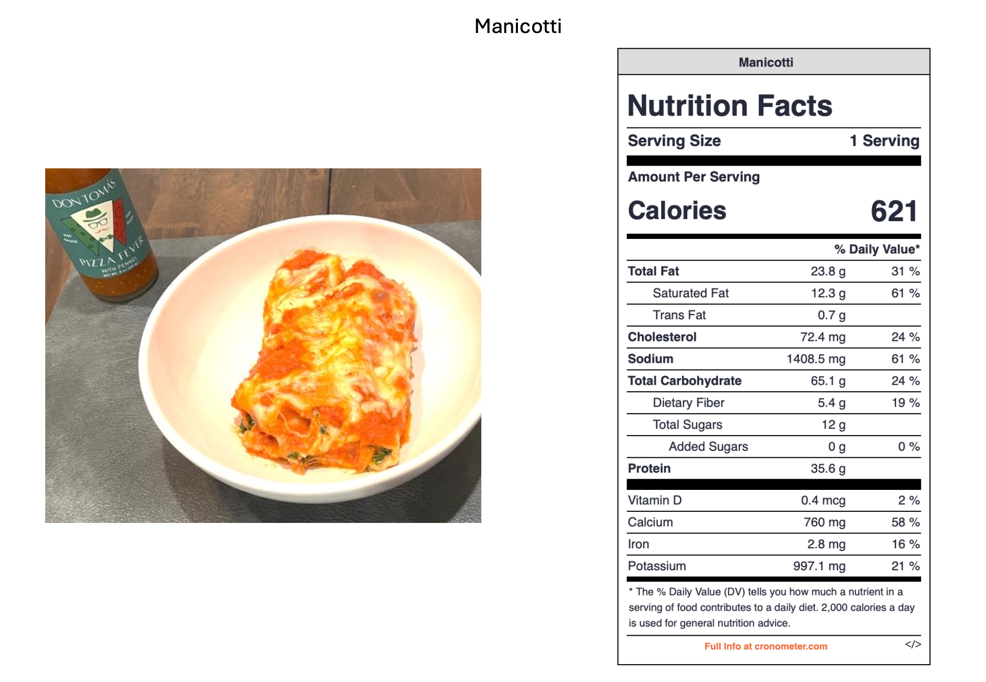 A plate of lasagna with cheese, tomato sauce, and spinach, placed on a table. A bottle of hot sauce labeled "Don Tom's Pizza Flavored" is positioned behind the plate.