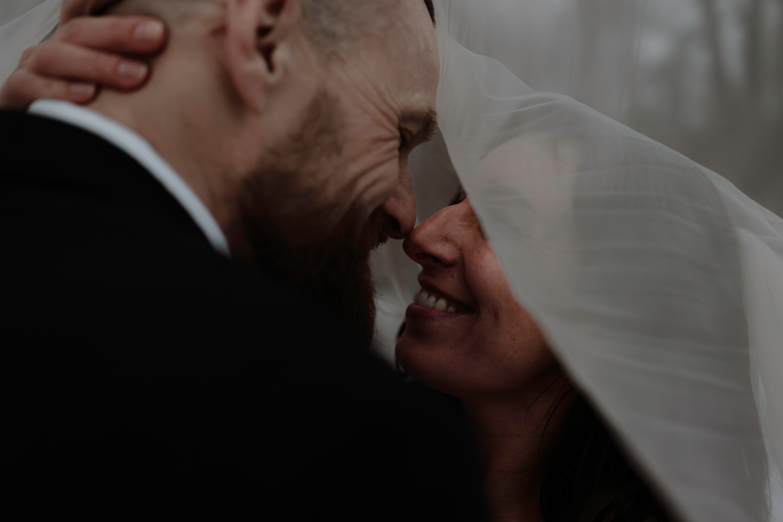 Intimate wedding photography portrait of a bride and groom touching noses under her veil.