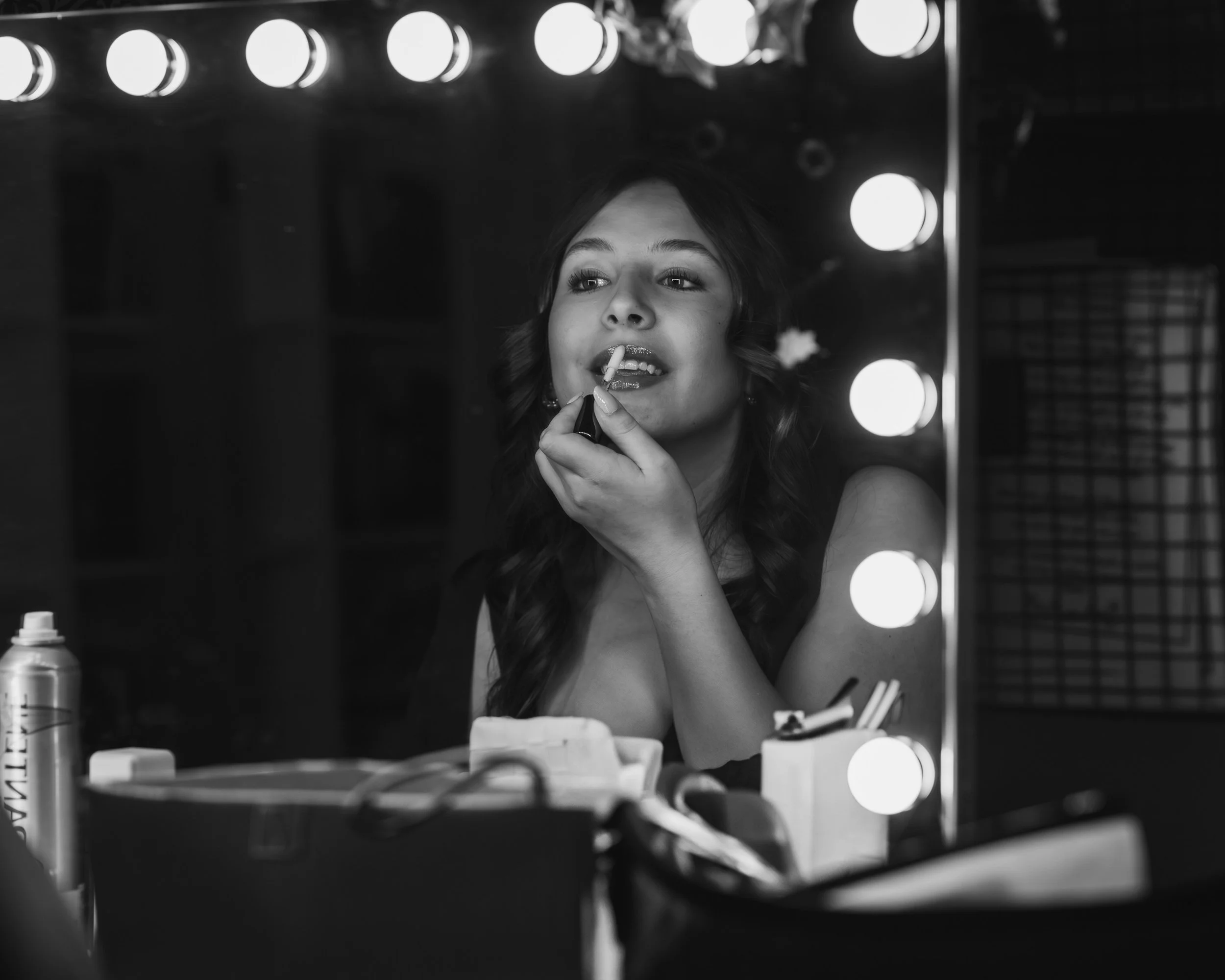 Authentic black and white wedding photography capturing a bride applying lipstick in a brightly lit vanity mirror.