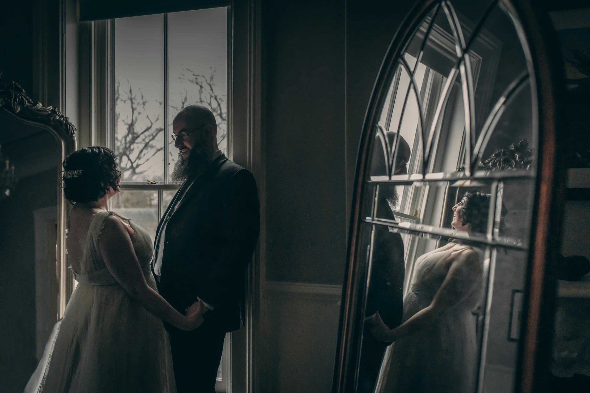 An artistic photo of the bride and groom's reflection in an ornate antique mirror, creating a moody and cinematic portrait.