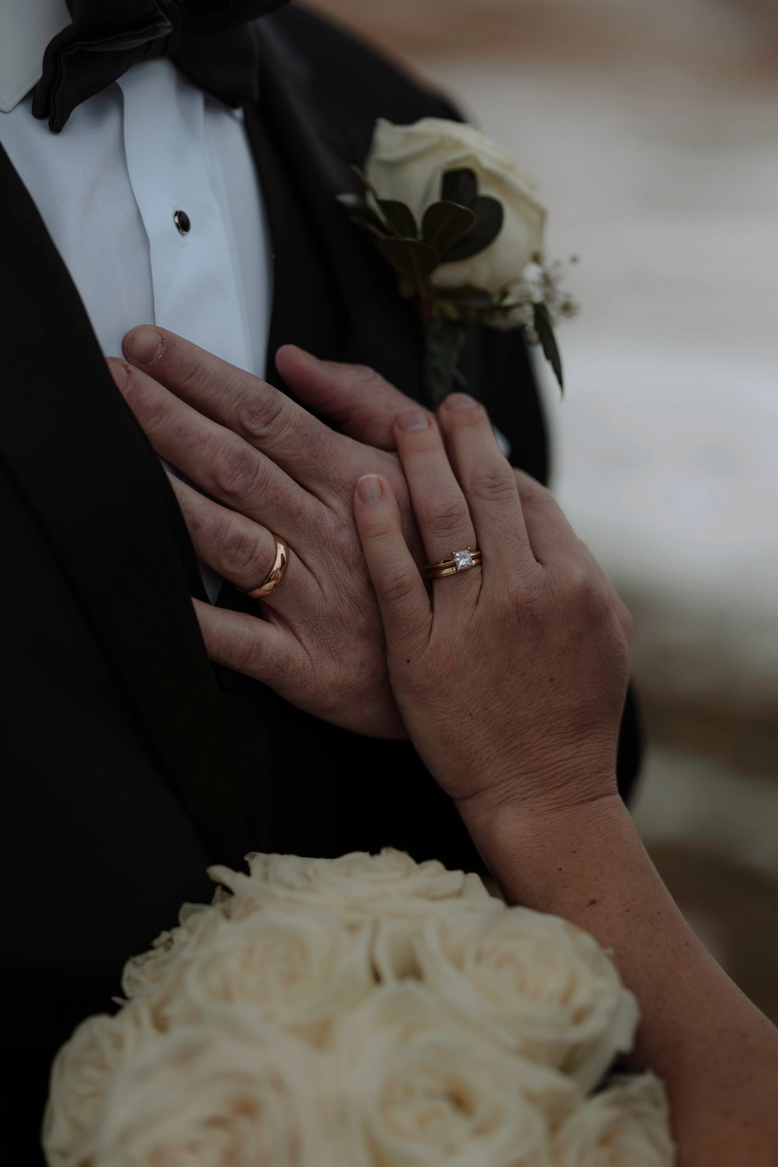 Still from a wedding film, capturing an intimate detail of a couple's hands and wedding rings with a bouquet.