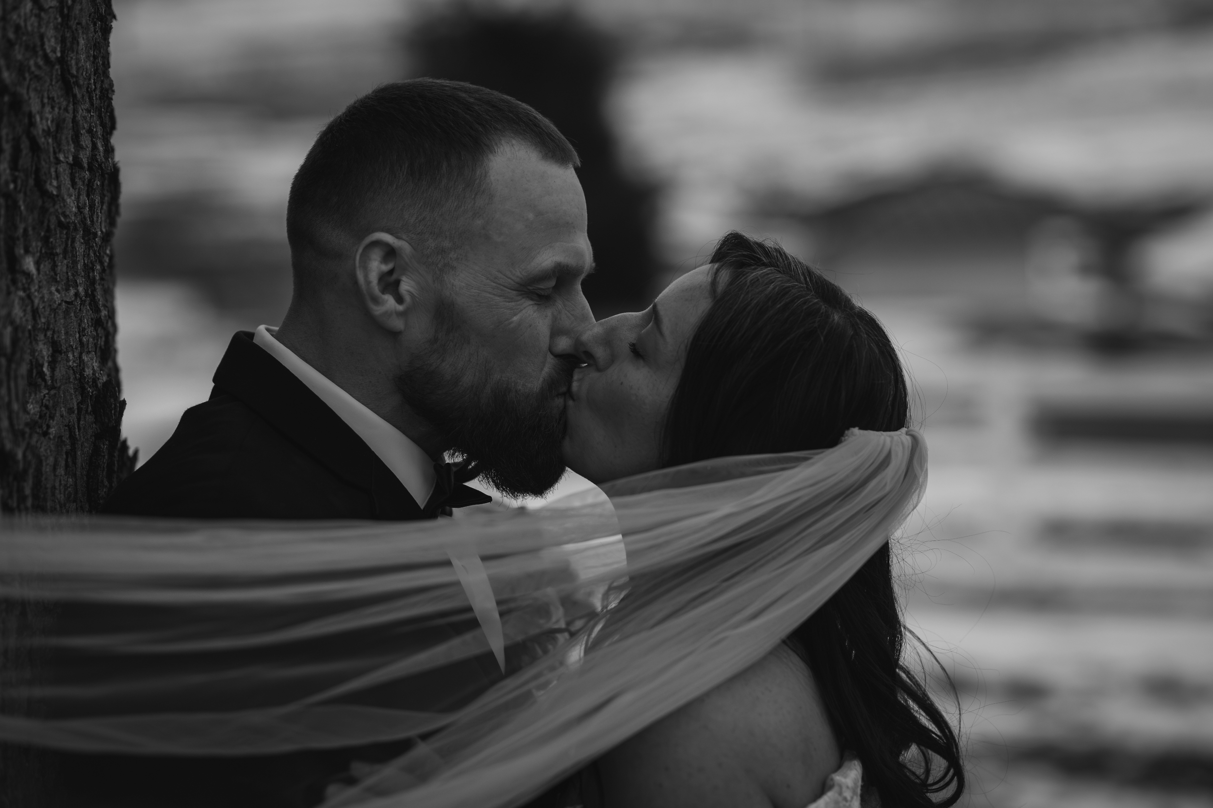 Intimate black and white wedding photography of a bride and groom kissing, with her veil elegantly wrapped around them.
