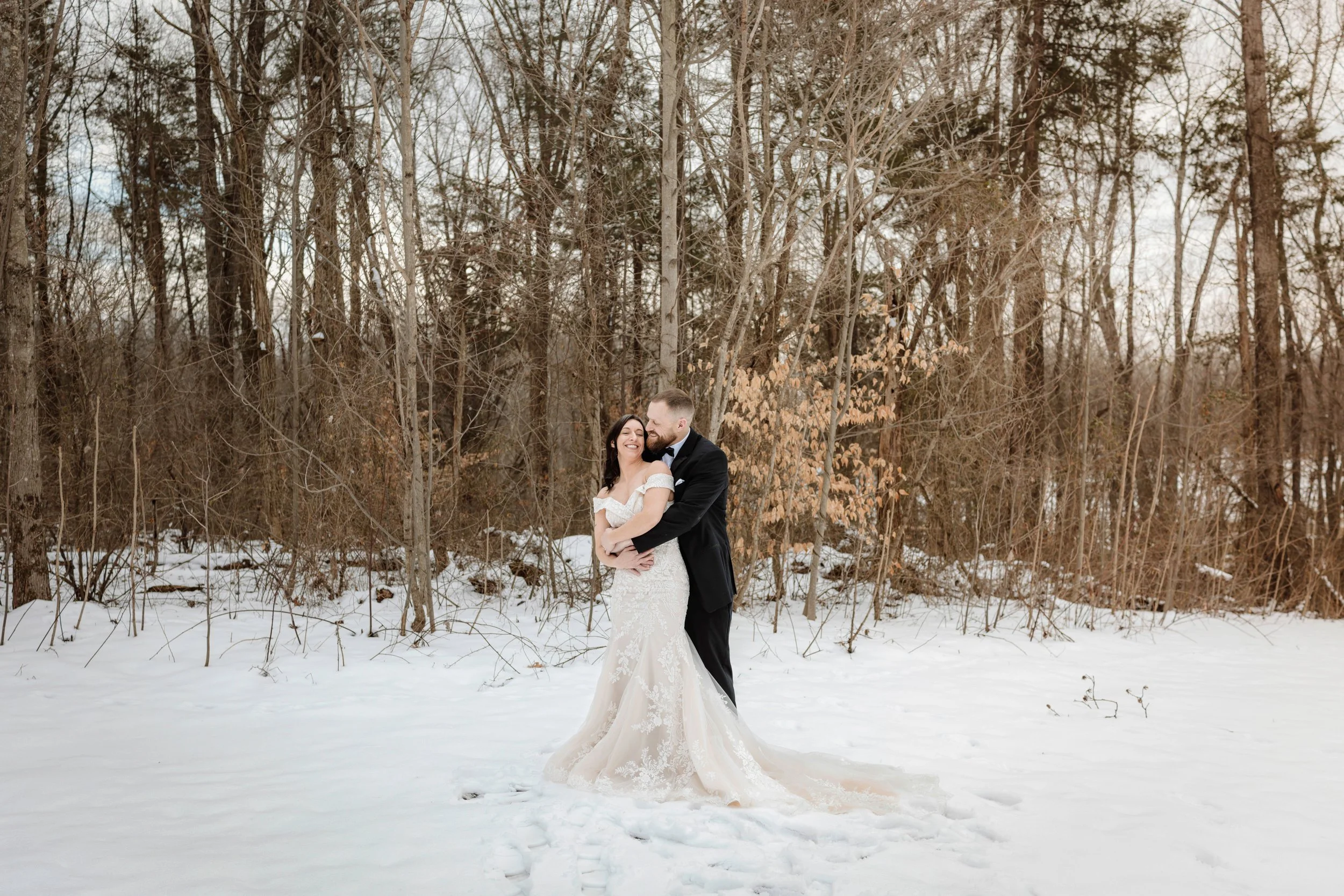 Romantic winter wedding photography of a bride and groom embracing and kissing in a beautiful snowy forest.