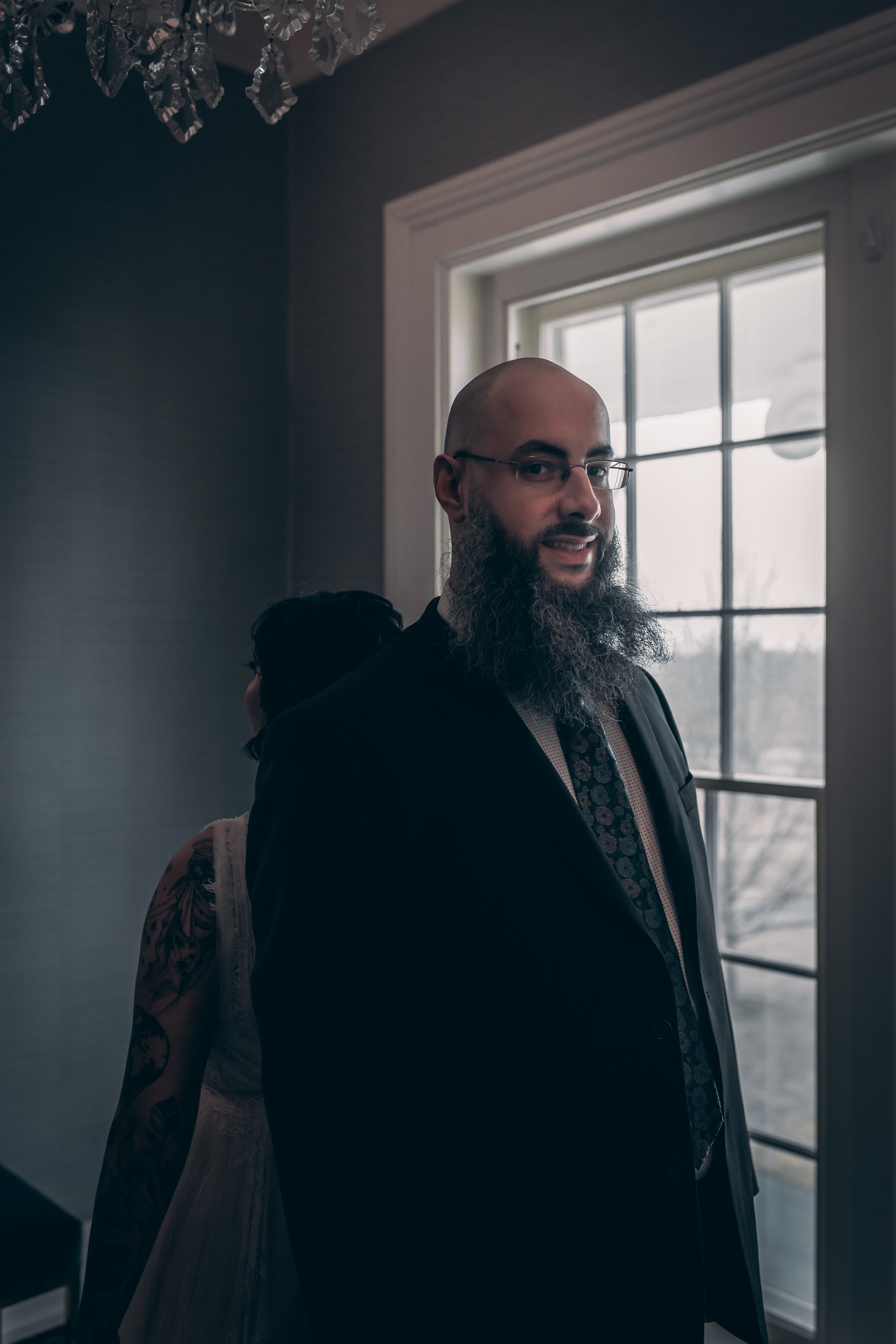 A classic and pensive portrait of the groom looking towards a window, lit by soft natural light on his wedding day.