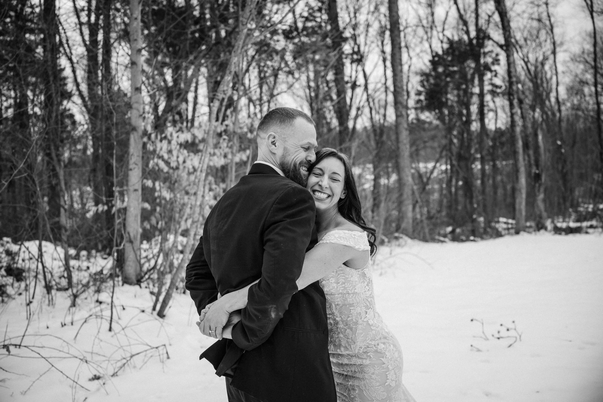 Joyful black and white wedding photography of a happy couple embracing in a snowy winter forest.