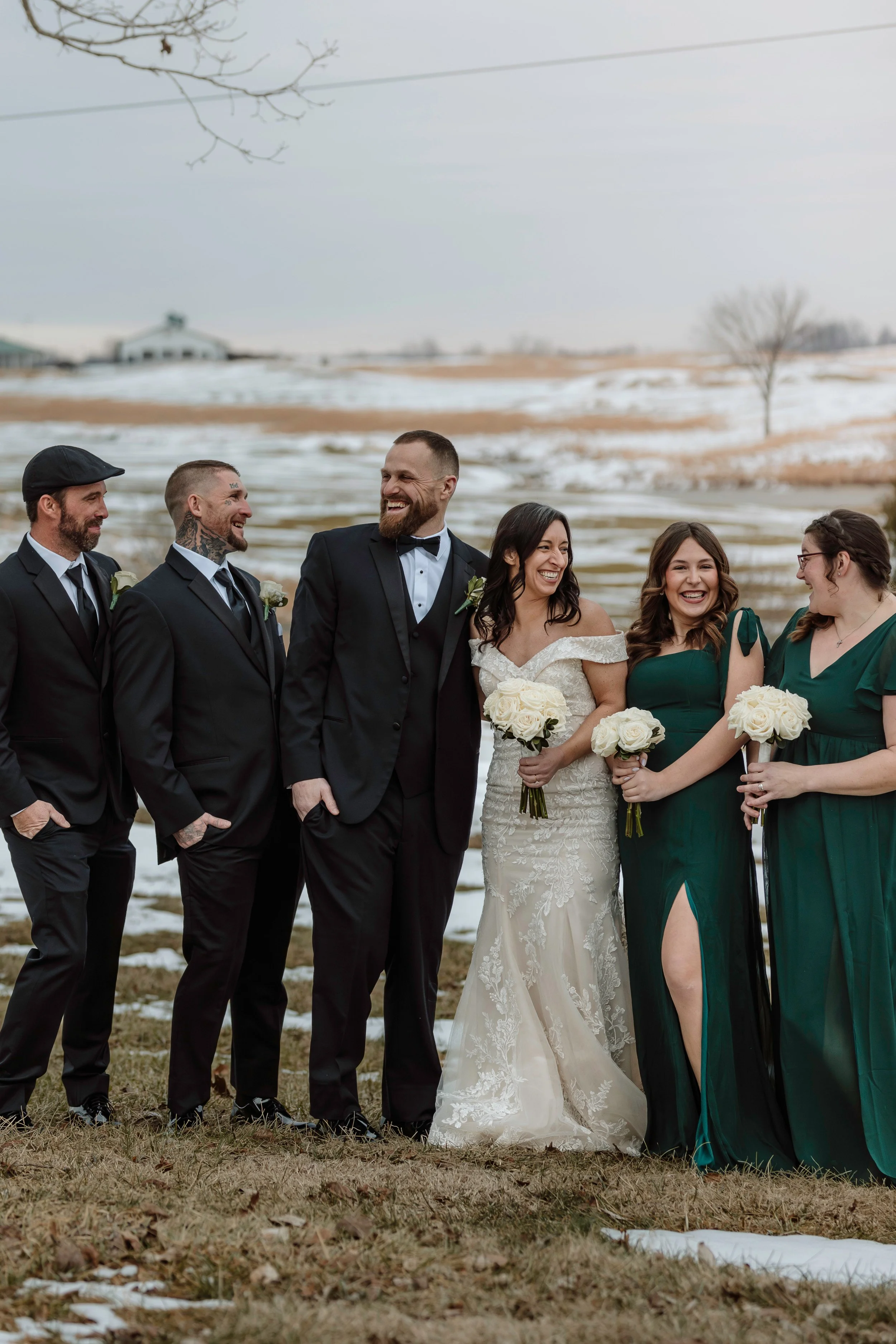 Smiling wedding party portrait with the bride, groom, and bridesmaids celebrating outdoors in a beautiful snowy setting.