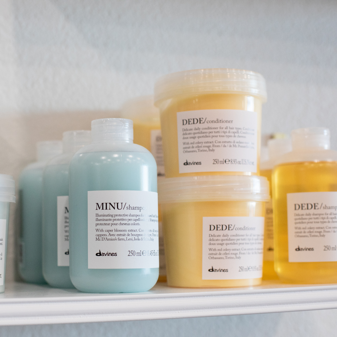 Various bottles and containers of hair products from the brand Davines, including MINU shampoo and DEDE conditioner, displayed on a shelf.