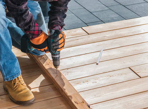 Person using a power drill to work on wooden planks outdoors.