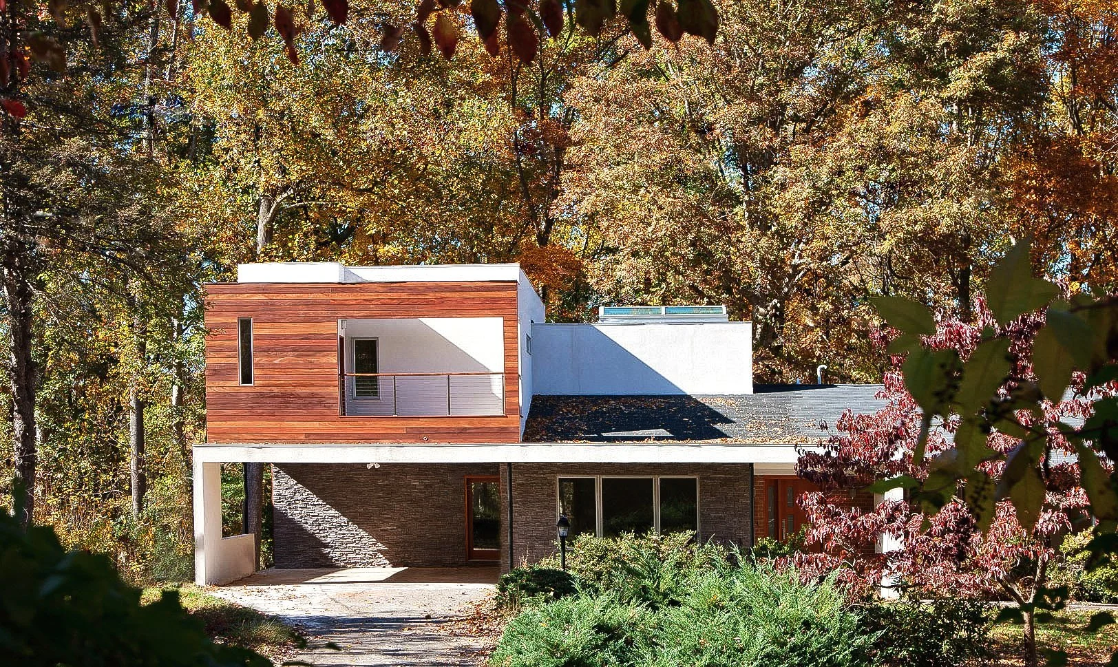 A modern house with a flat roof framed by colorful autumn trees and bushes.