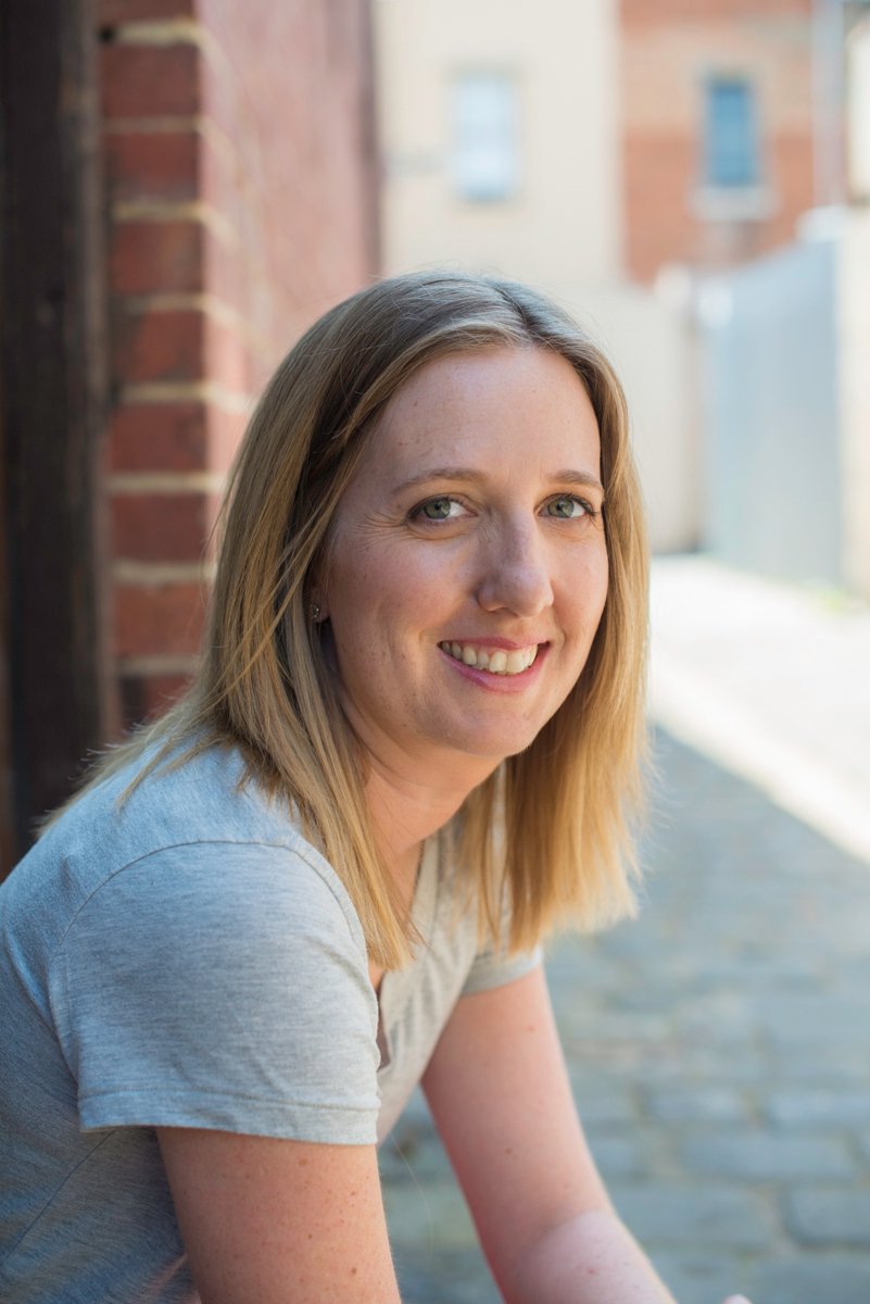 Photo of Leesa sitting near a brick wall smiling.