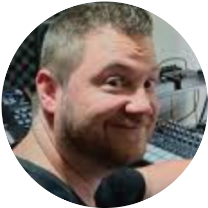 A man with short blond hair and a beard, smiling and looking at the camera in an office or radio studio setting.