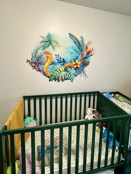 Interior of a baby crib with stuffed animals, against a white wall decorated with a colorful jungle animal mural.