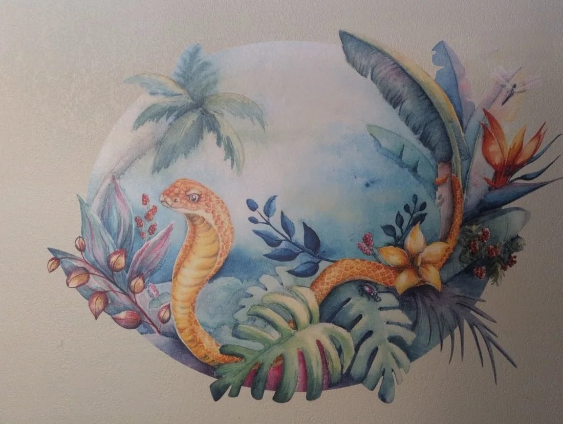 Watercolor painting of a tropical scene with a snake, palm trees, and large leaves. It is printed on fabric and installed as a mural on a textured bedroom wall.