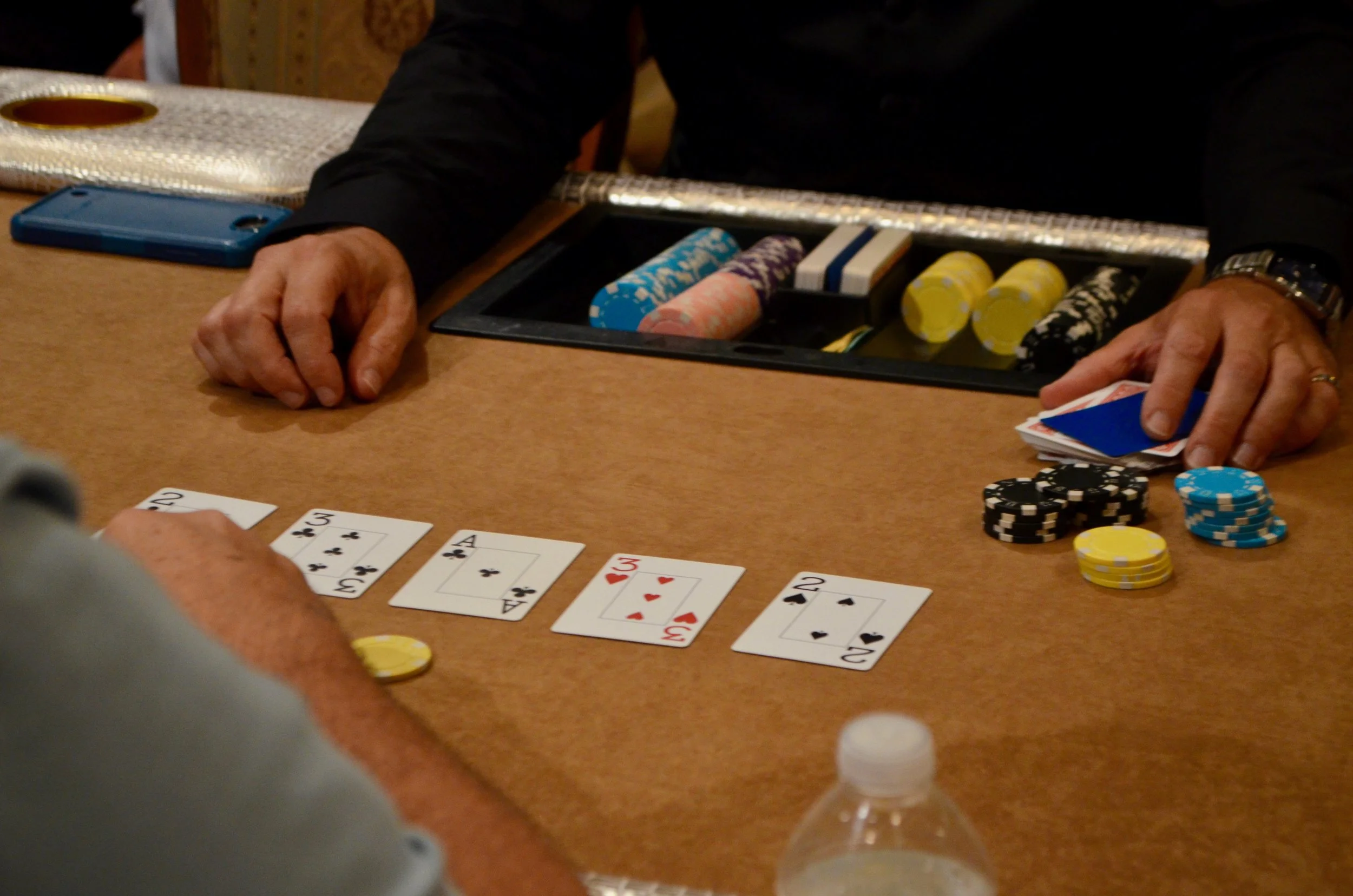 Close-up of a person's hands at a poker table, with playing cards and poker chips in front of them, during a game.