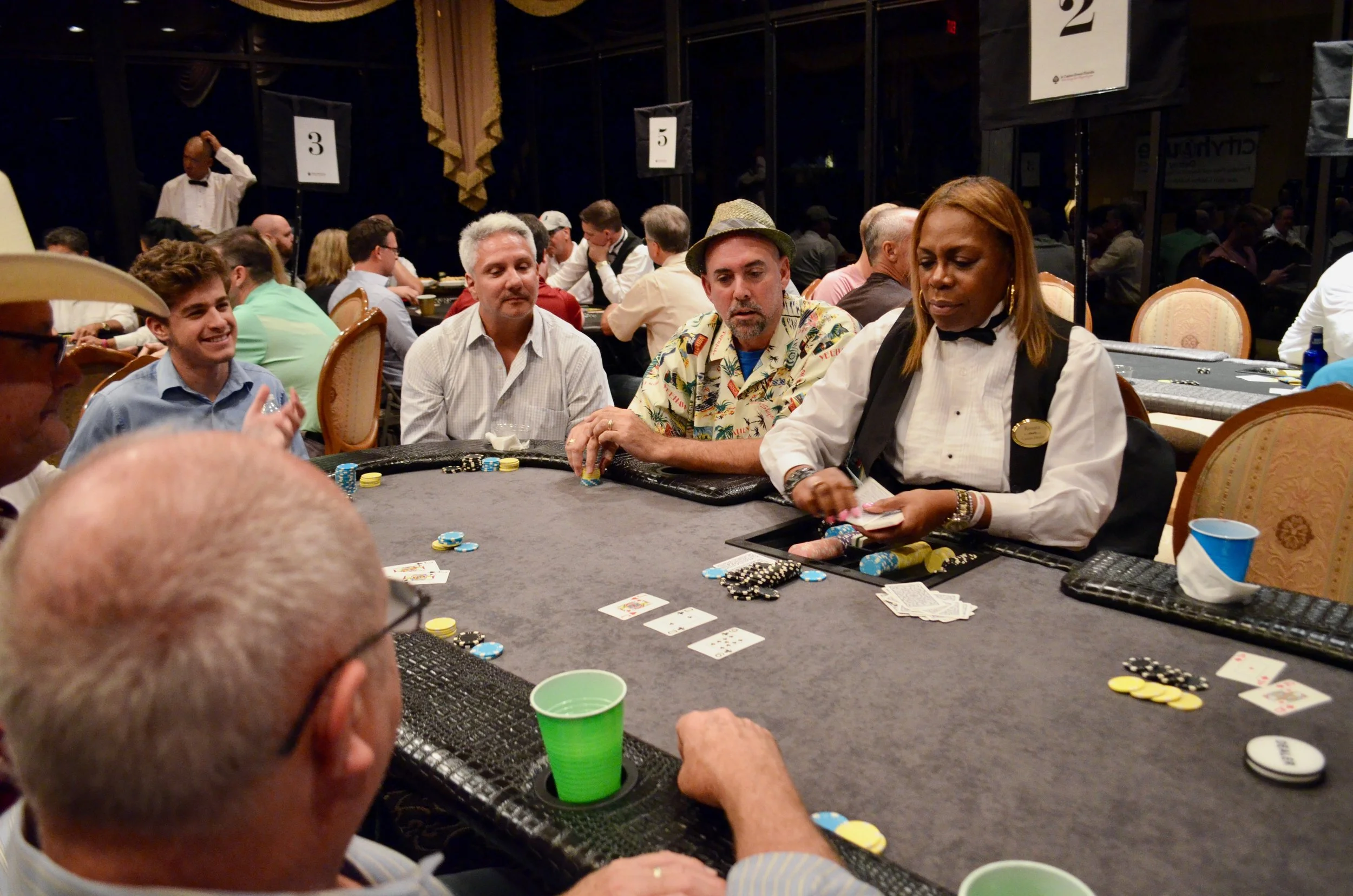 People playing poker at a casino table with chips, cards, and a dealer in the foreground.