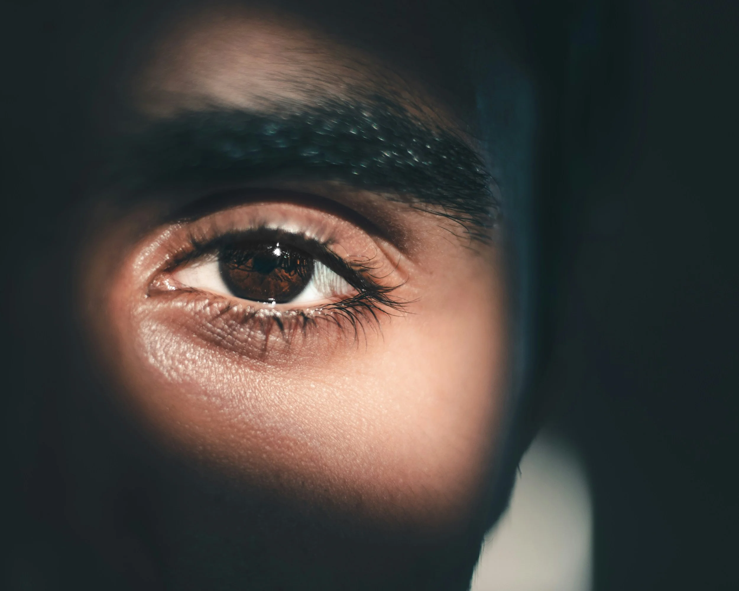 Close-up of a person's eye with dark brown iris, long eyelashes, and smooth skin.