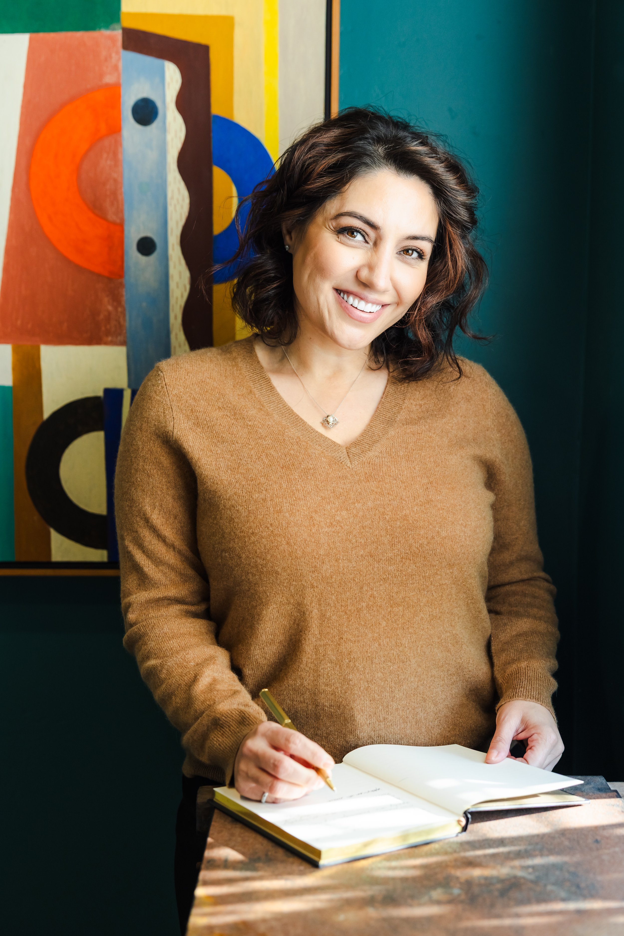 Atti Moricelli, therapist at Grey Insight, smiling while signing a book, standing in front of an abstract colorful painting.