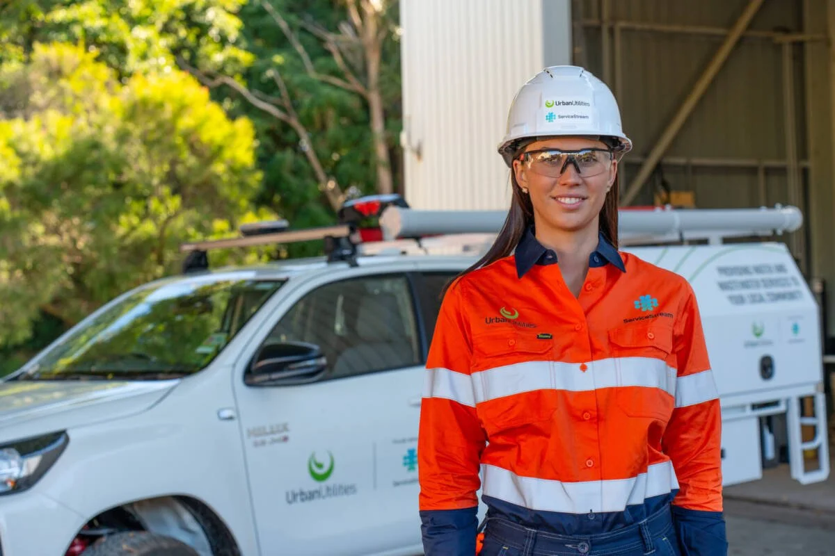 Young woman in high-vis workgear and hardhat, in front of a Service Stream vehicle