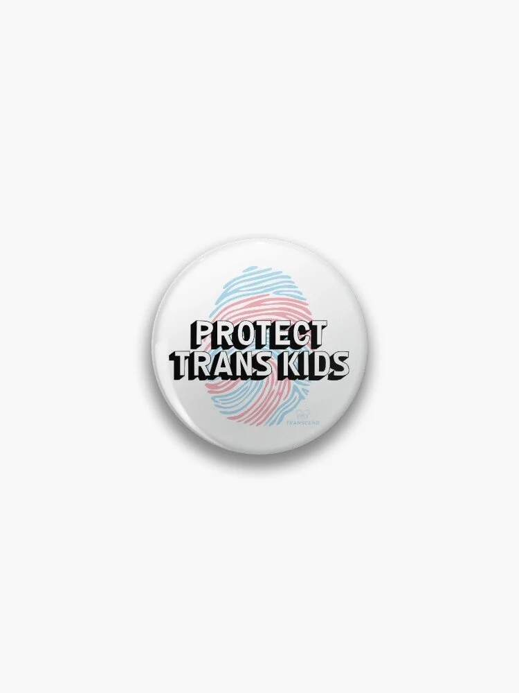 badge with the words 'protect trans kids' in the trans flag colours