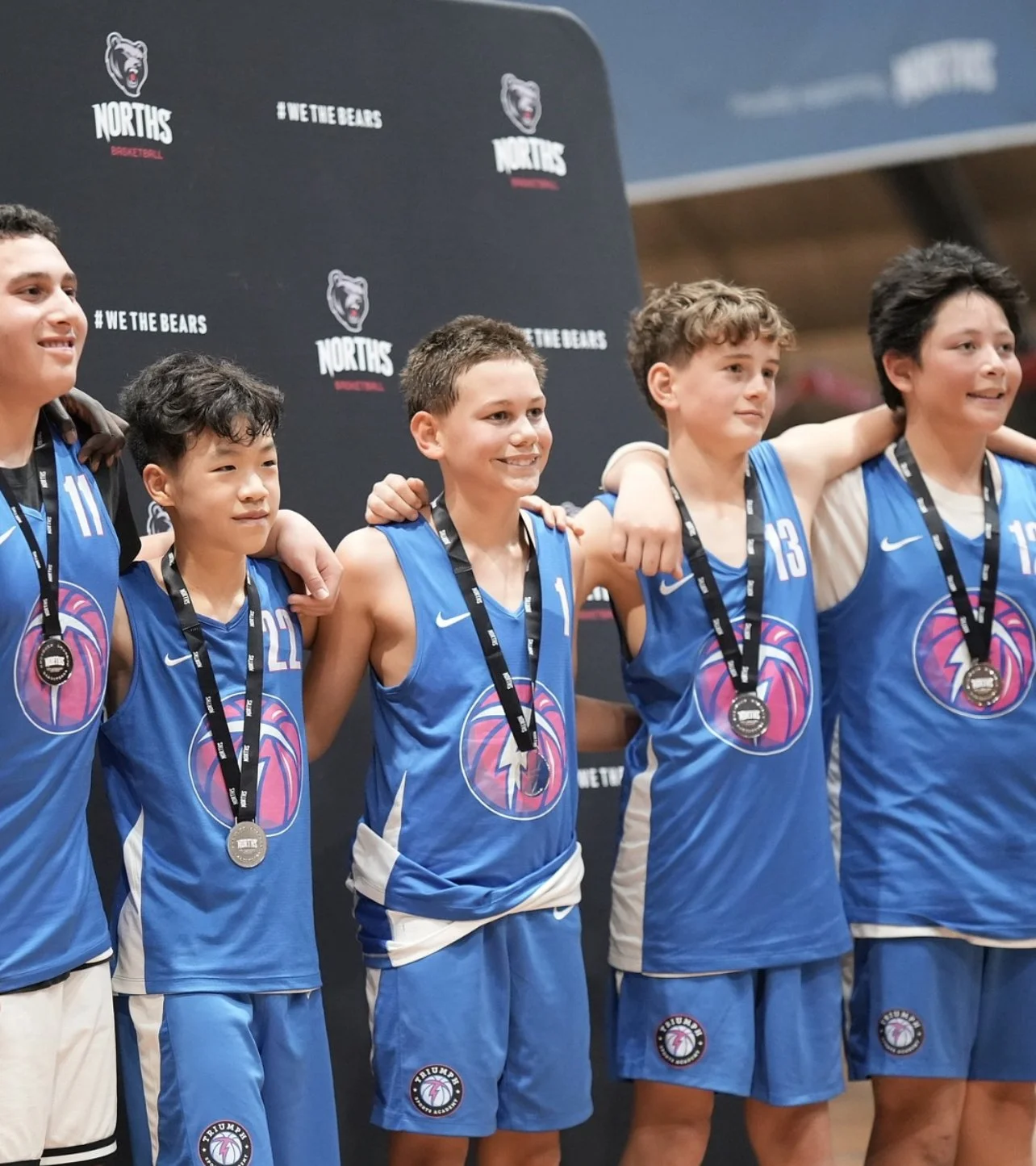 Group of young basketball players in blue uniforms celebrating with medals after a game, standing with arm around each other at a team event.