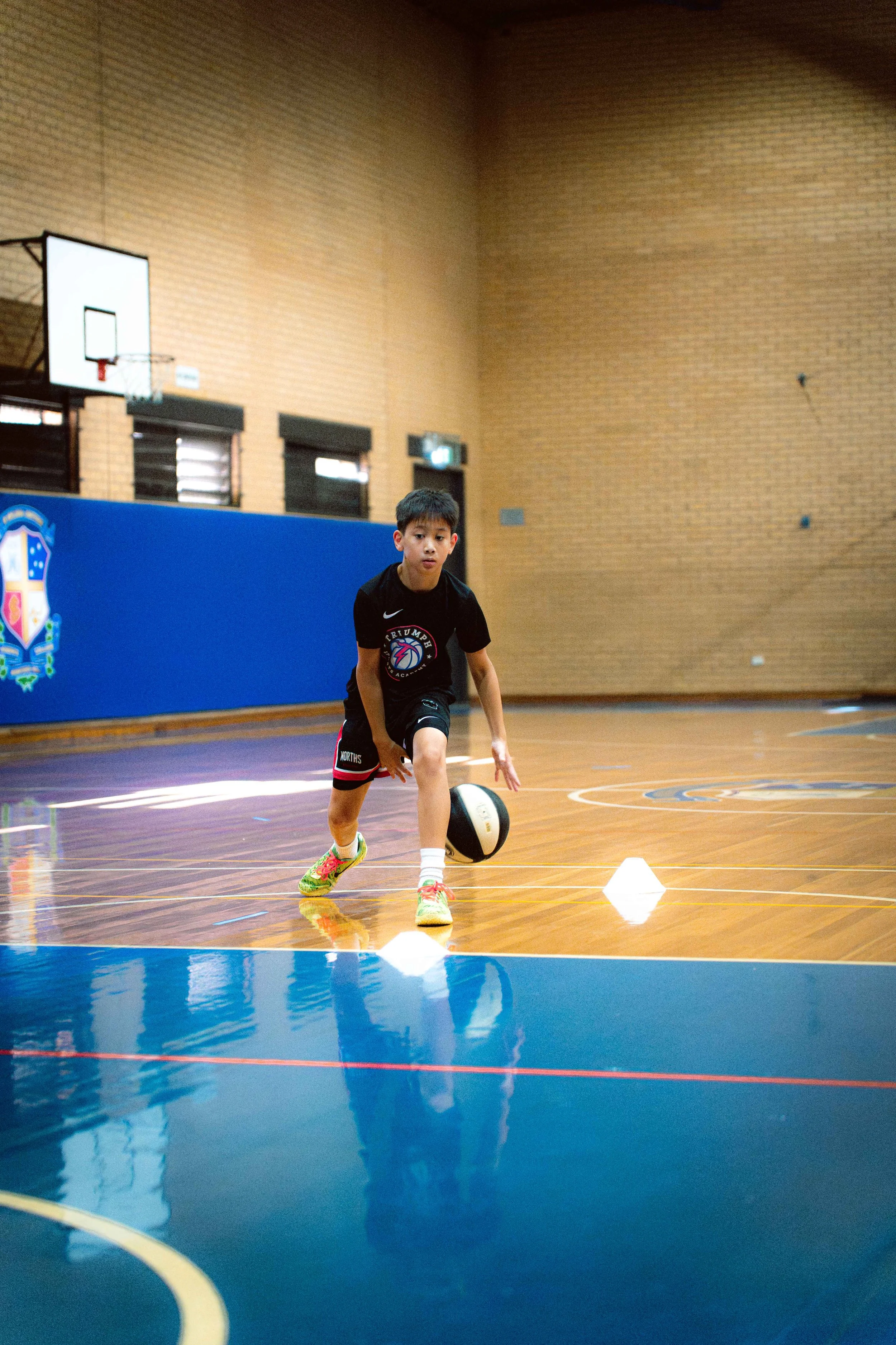Young boy playing with a basketball on an indoor court, dribbling around small cones as part of a training drill.