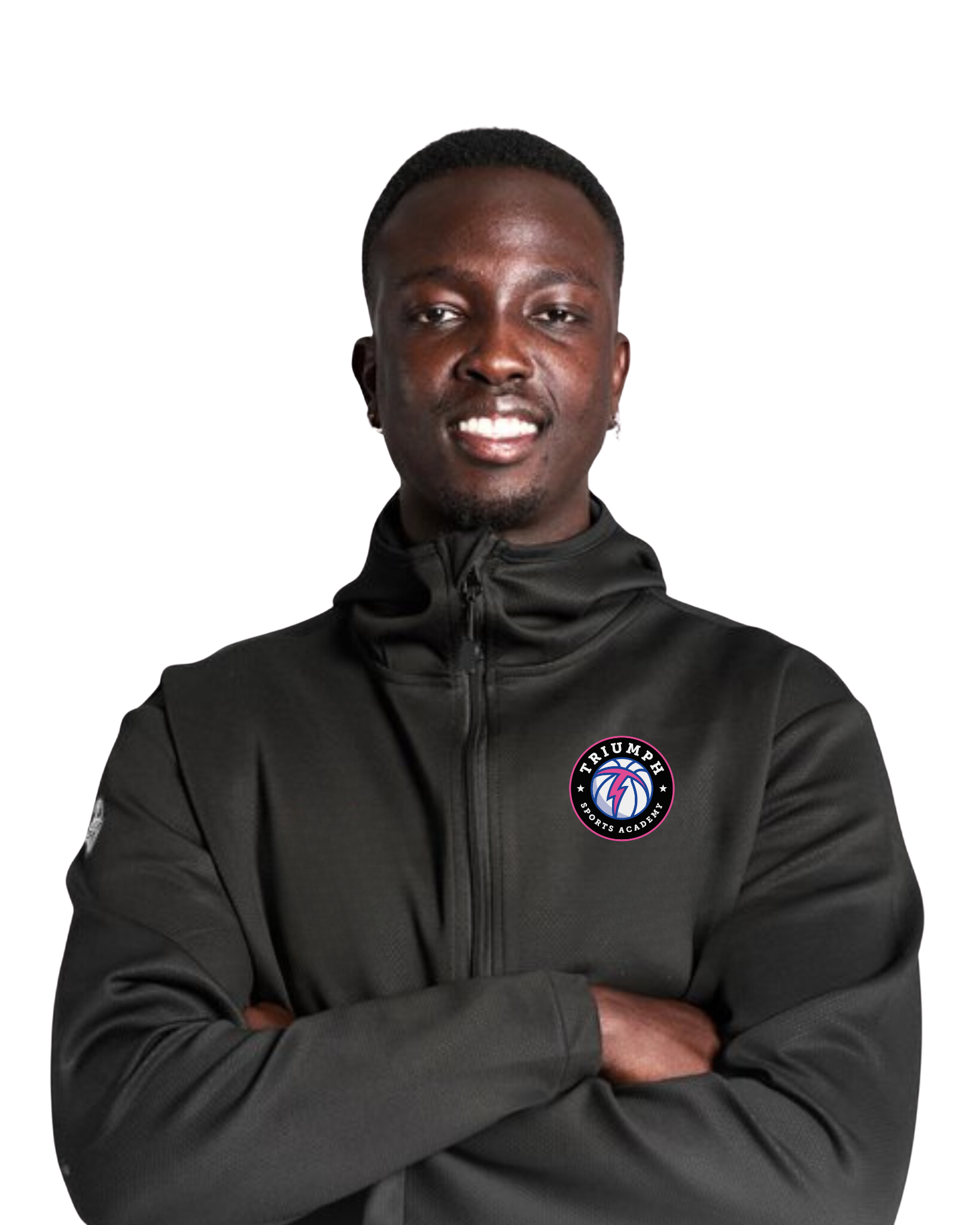 A young Black man with short hair smiling, wearing a black zip-up sports jacket with the Triumph Sports Academy logo on the chest, arms crossed.
