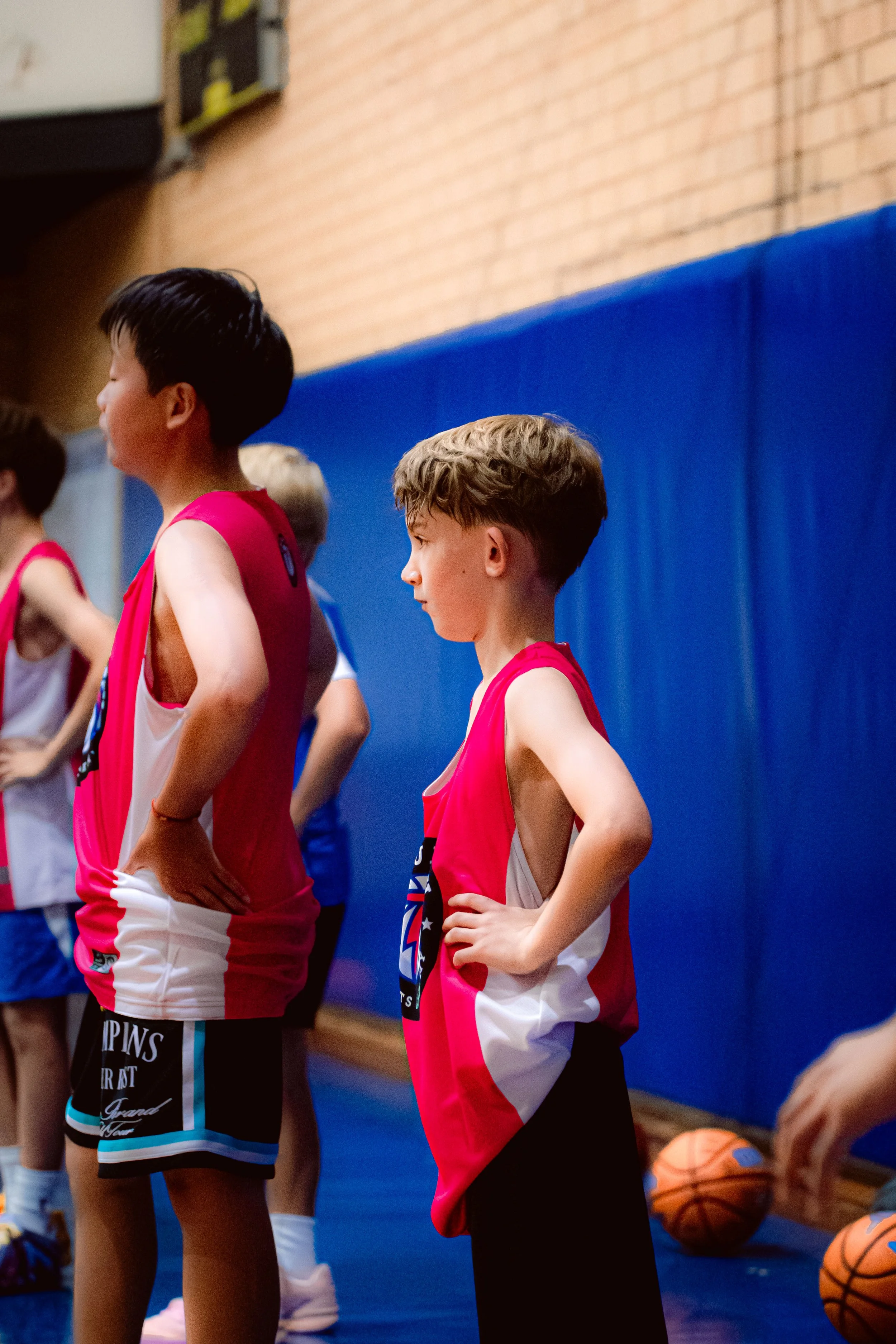 Young boy playing with a basketball on an indoor court, dribbling around small cones as part of a training drill.
