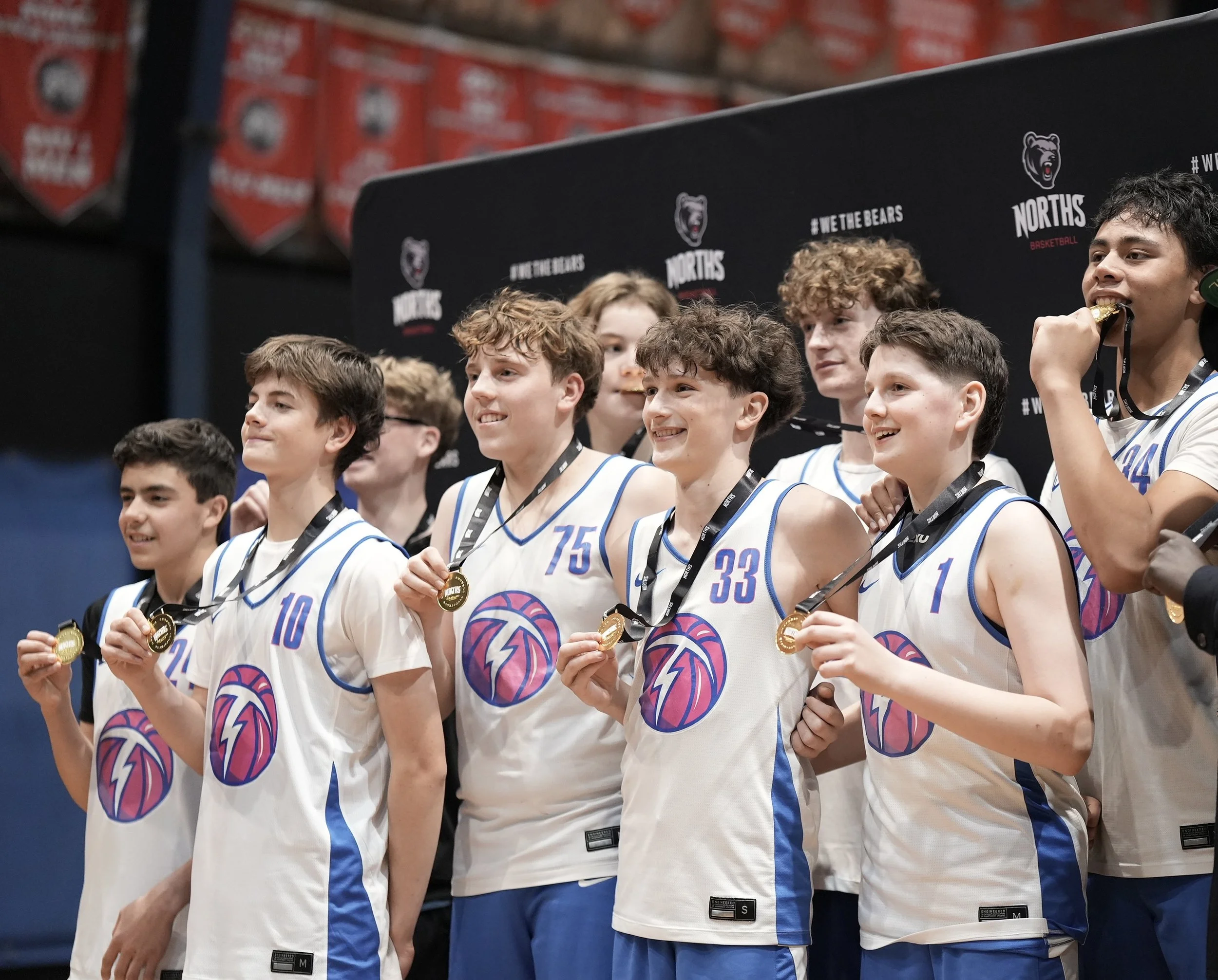 Young basketball players in white jerseys with blue accents, holding medals at an awards ceremony.