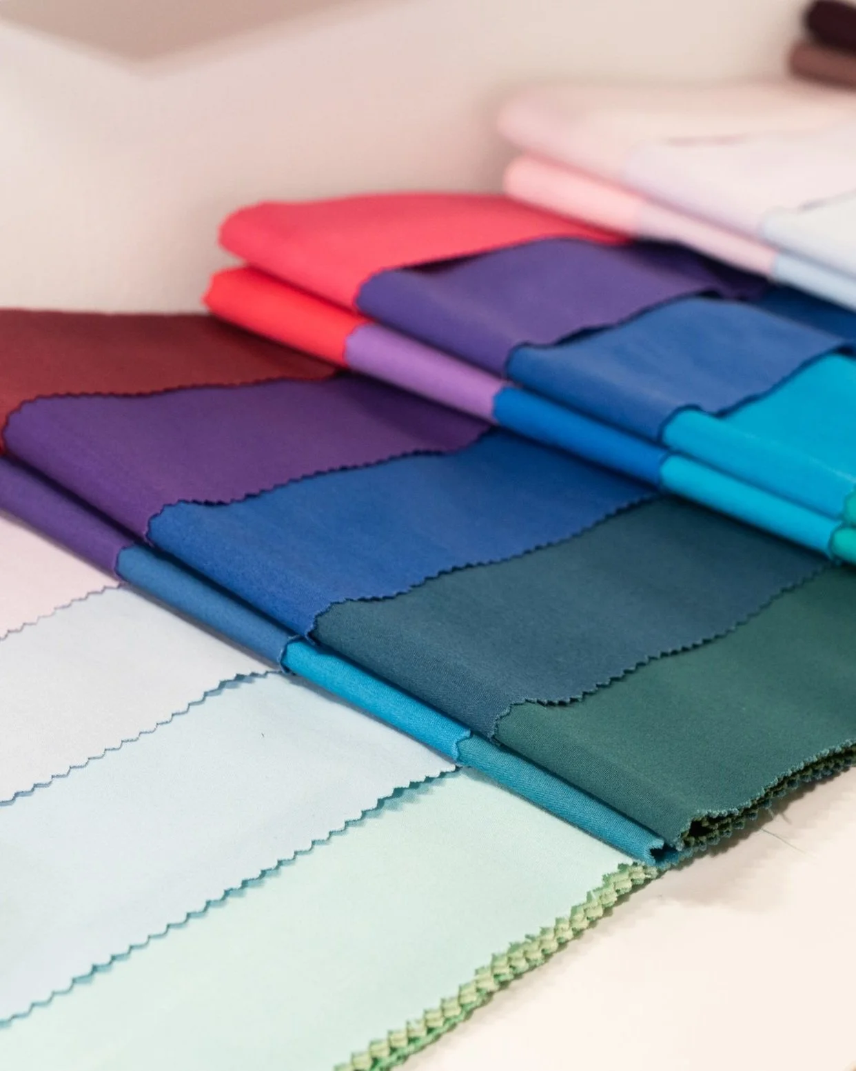 An assortment of folded fabric swatches in various colors including purple, blue, teal, pink, and white, arranged on a flat surface.
